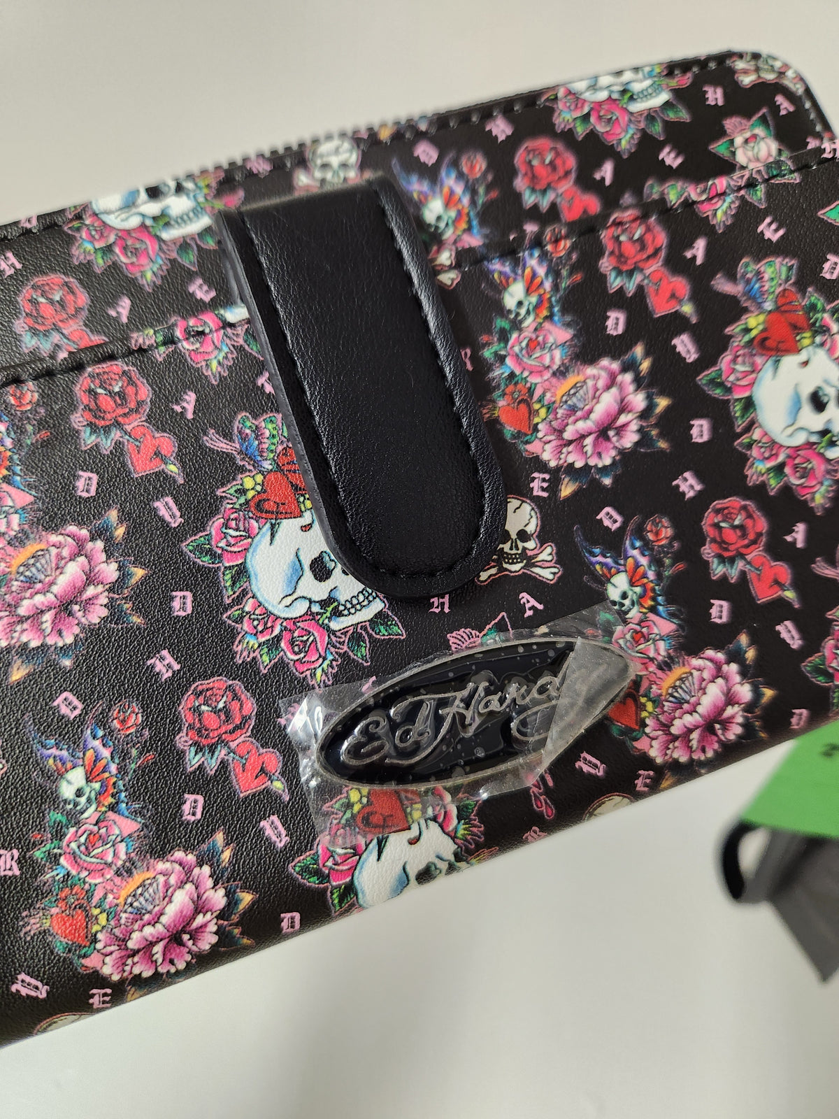 Ed Hardy Skull and Rose Tattoo Print Wallet feature a classic Y2K-inspired tattoo graphic pattern with skulls and pink flowers, complete with a silver metallic Ed Hardy brand logo plate on the front.
