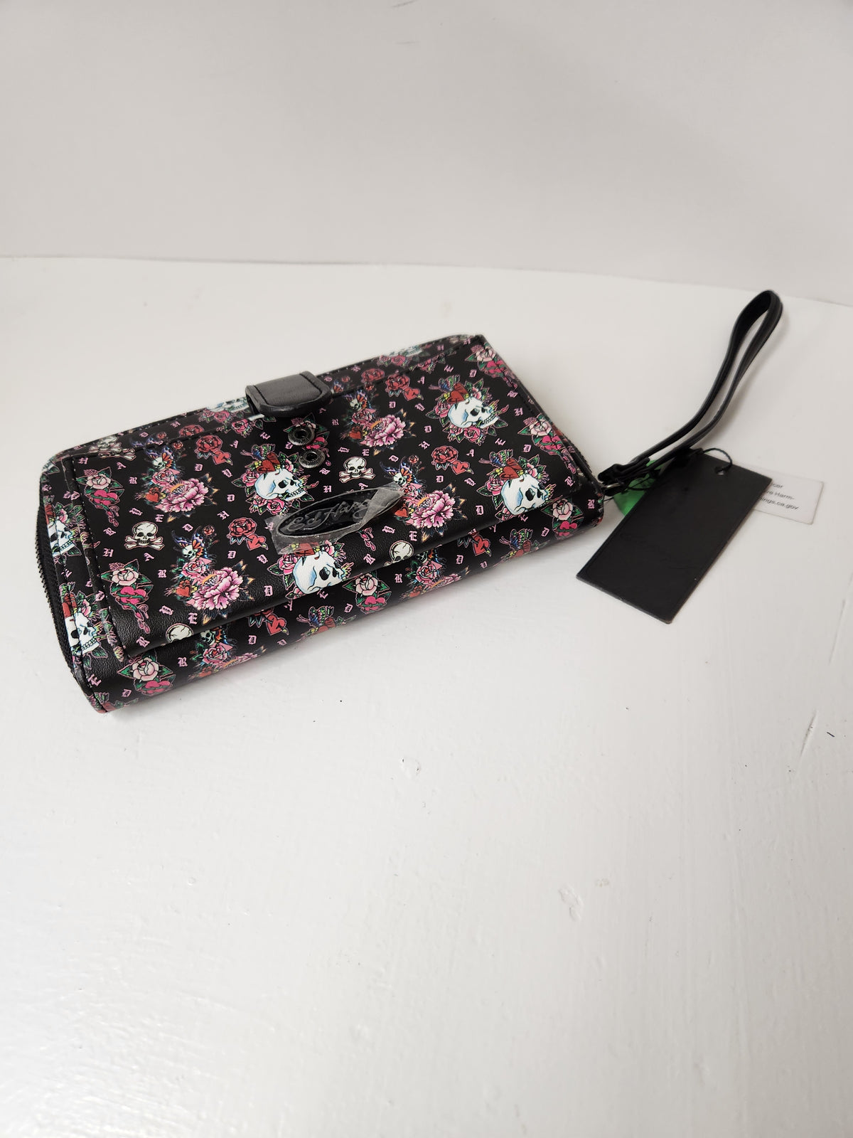 Ed Hardy Skull and Rose Tattoo Print Wallet feature a classic Y2K-inspired tattoo graphic pattern with skulls and pink flowers, complete with a silver metallic Ed Hardy brand logo plate on the front.