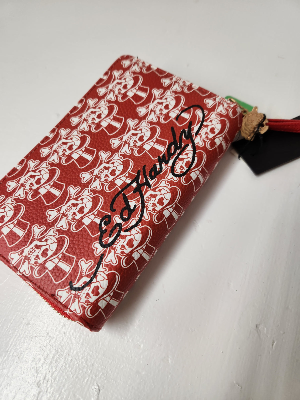  Ed Hardy wristlet wallet features a full zip-around closure, card slot organizers, a zippered coin pocket, and a detachable wristlet strap. Prominent rhinestone-embellished roaring tiger head centered among traditional tattoo flash graphics, including a winged Pegasus and skulls.