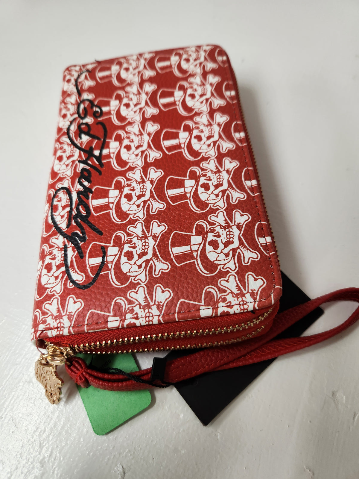  Ed Hardy wristlet wallet features a full zip-around closure, card slot organizers, a zippered coin pocket, and a detachable wristlet strap. Prominent rhinestone-embellished roaring tiger head centered among traditional tattoo flash graphics, including a winged Pegasus and skulls.