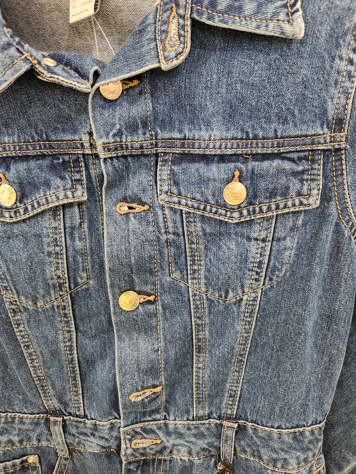 Close-up of a blue denim jacket with gold-tone metal buttons and contrast stitching.