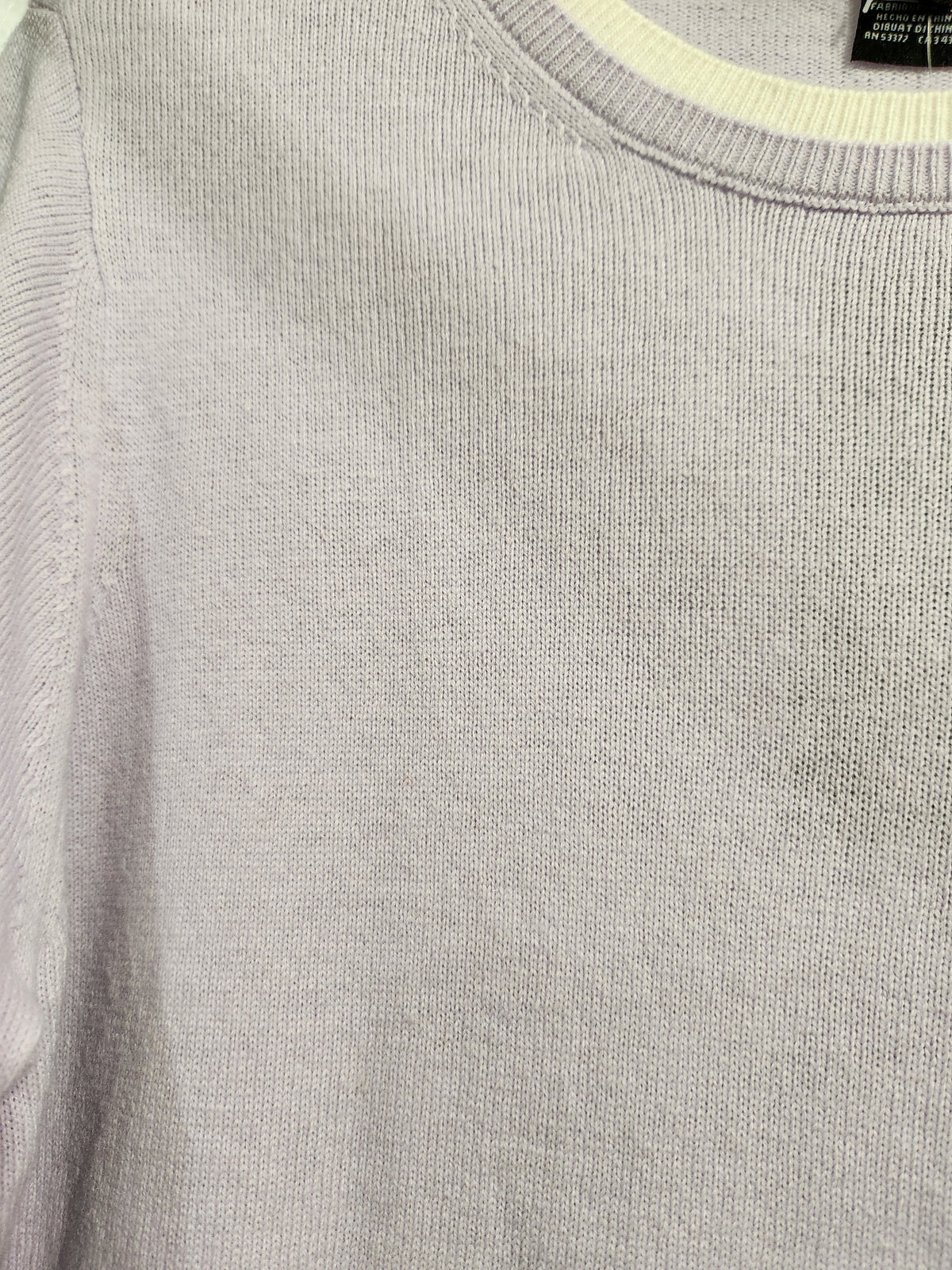 Close-up of a light gray ribbed knit sweater with a cream-colored inner collar lining.