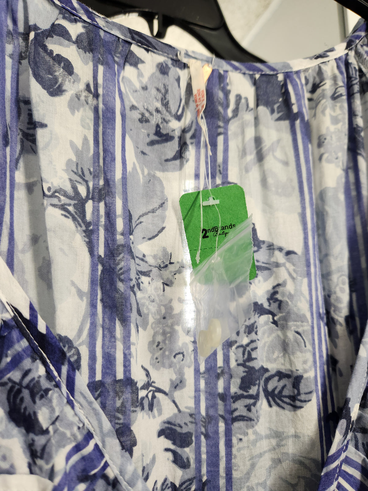 A close-up of a lightweight white blouse with a blue floral and vertical stripe pattern, hanging on a black hanger with a green price tag attached.