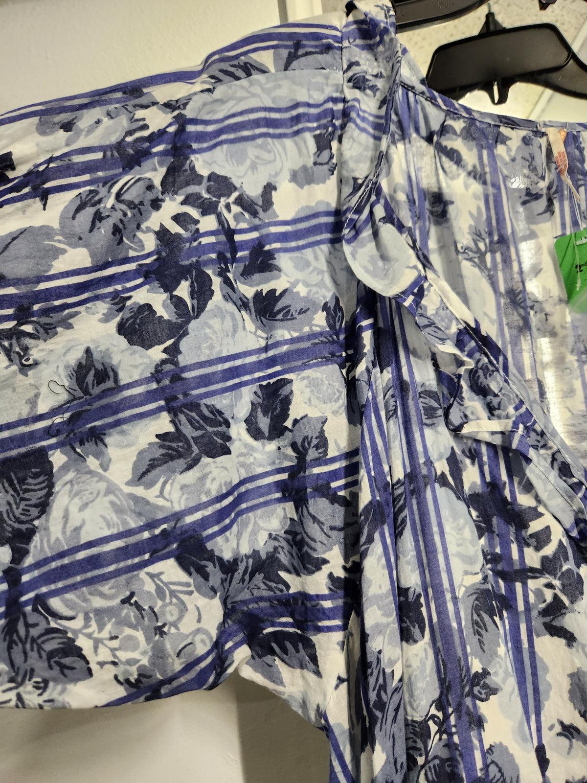A lightweight white wrap shirt with a blue floral and striped pattern, hanging on a black hanger.