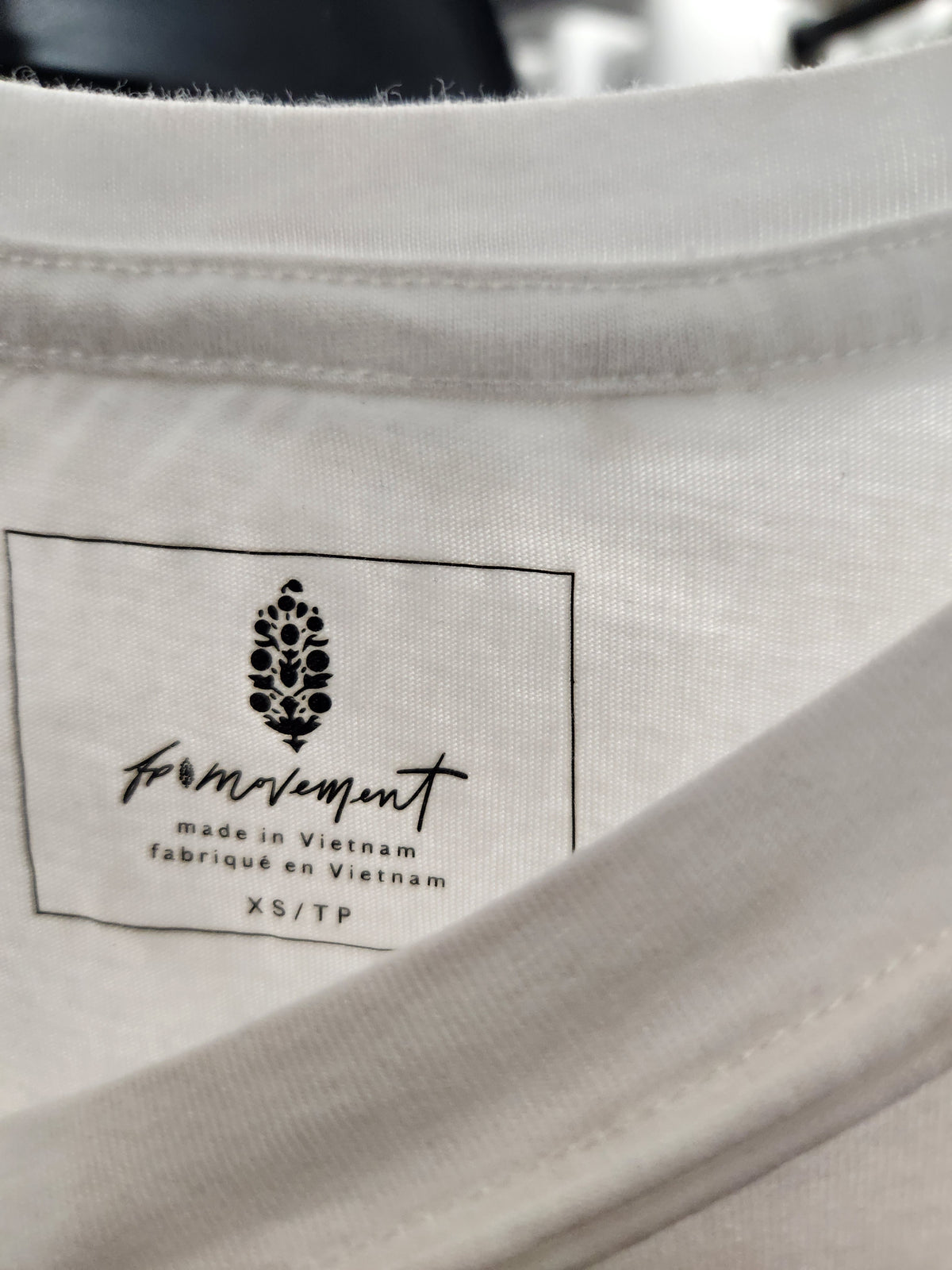 Close-up of the inside collar of a white t-shirt showing a sewn-in brand label for 'formvment' with 'made in Vietnam' and size 'XS/TP'.
