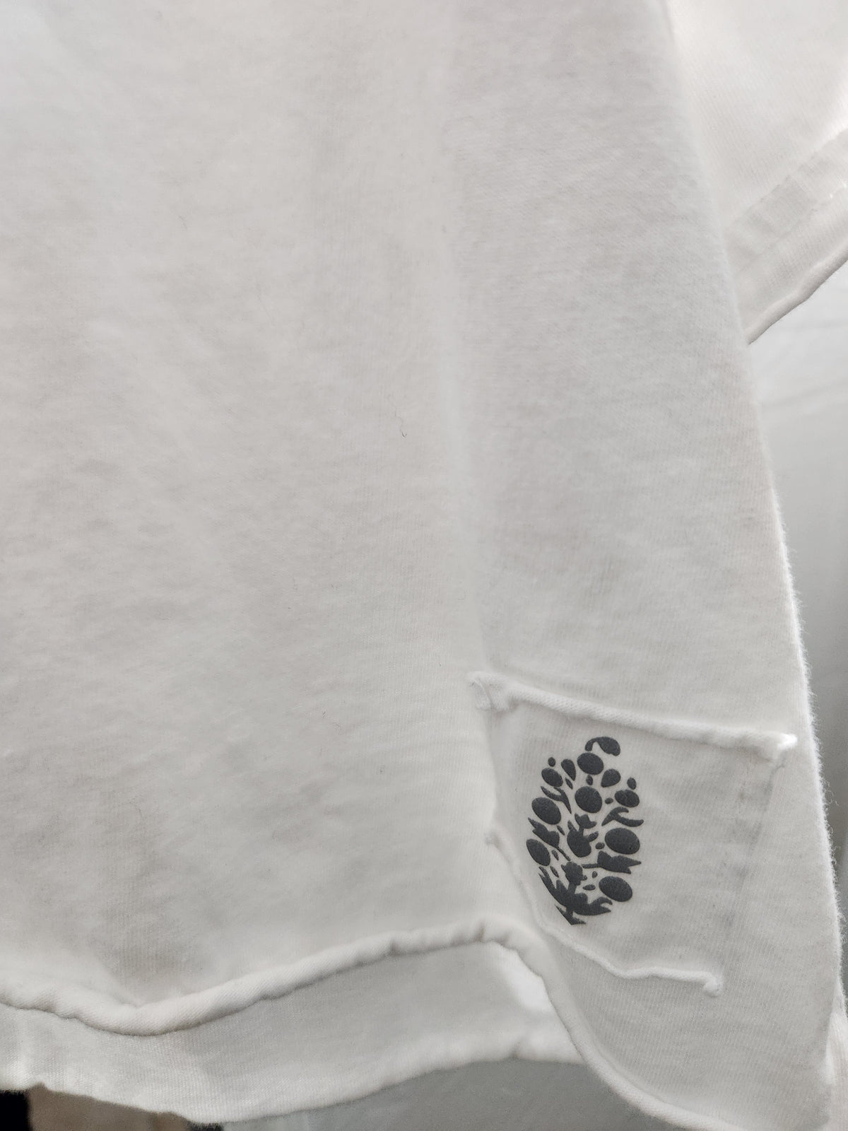 Close-up of a white fabric garment, likely a sweatshirt or hoodie, showing a small black embroidered or printed floral patch near the hem.