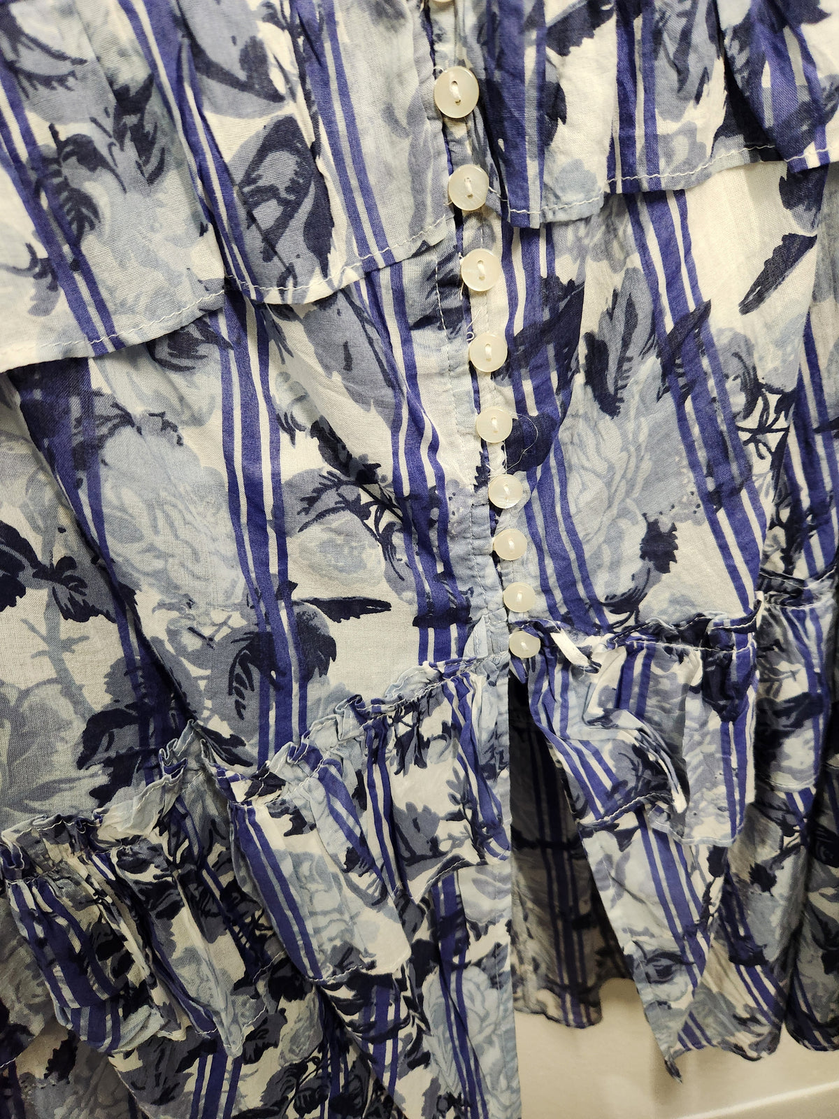 A close-up of a ruffled button-front garment with a blue and white tropical print featuring palm trees and vertical stripes.