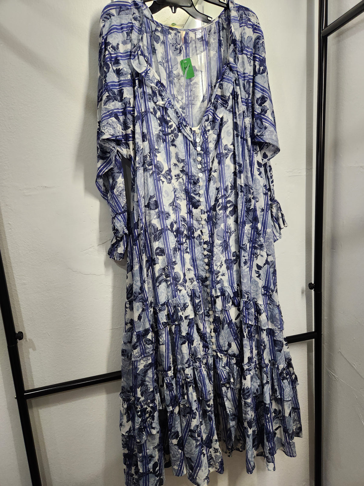 A long-sleeve bohemian-style maxi dress with a blue and white floral print, hanging on a black hanger against a white wall.