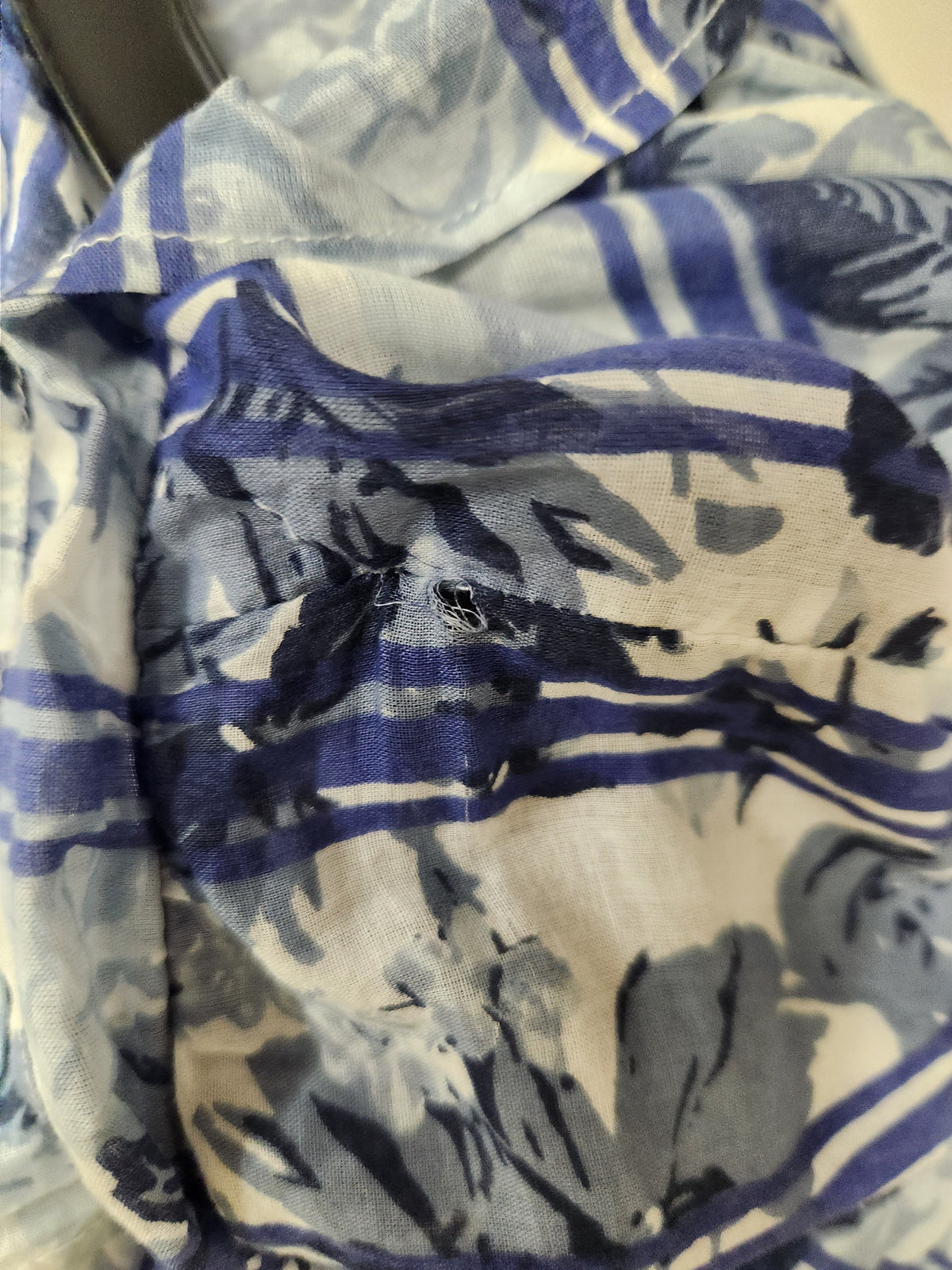 Close-up of a lightweight fabric with a blue and white floral and stripe pattern, showing a small hole near the center.