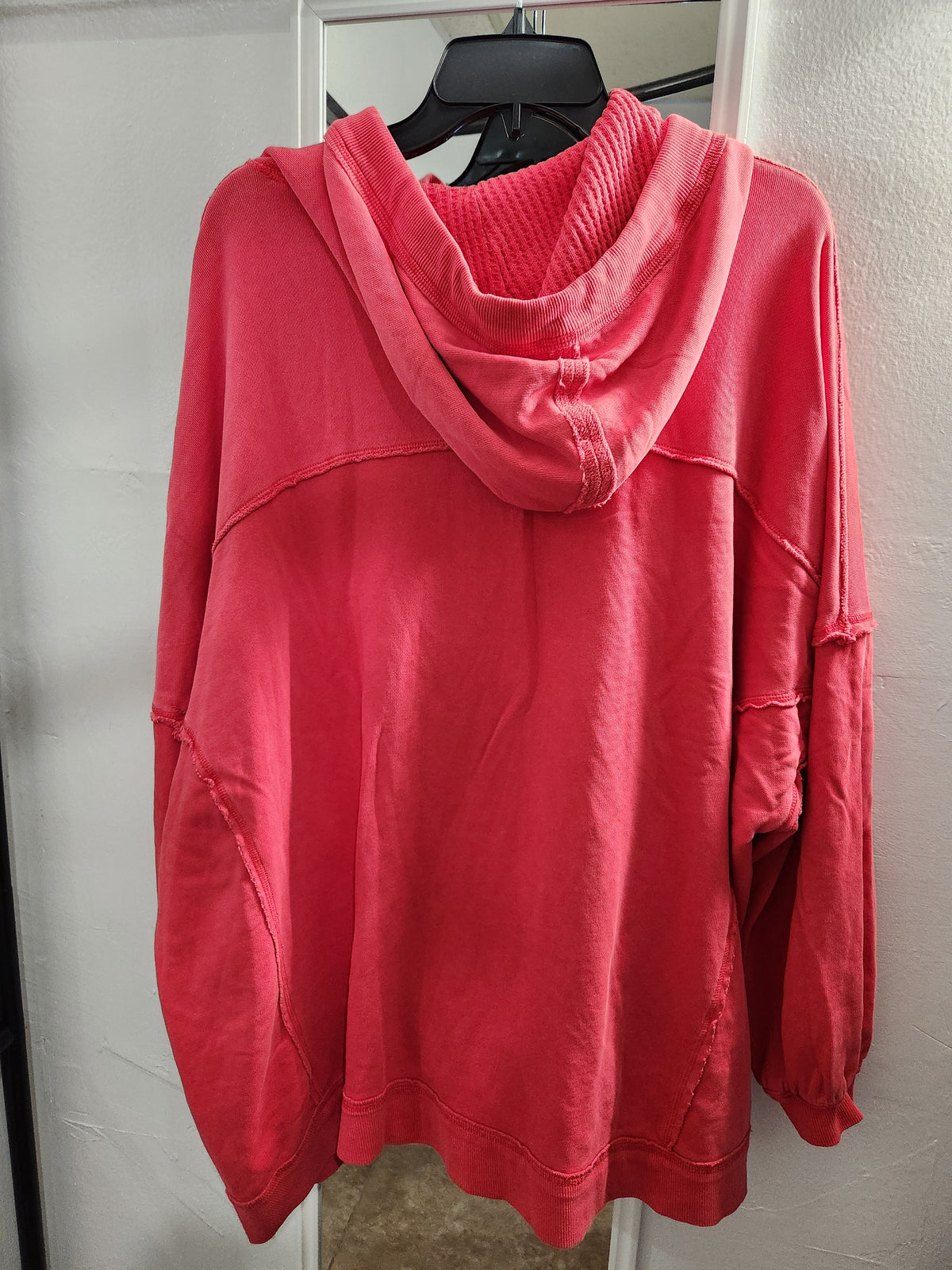 A coral pink hooded sweatshirt hanging on a black hanger against a white door frame.