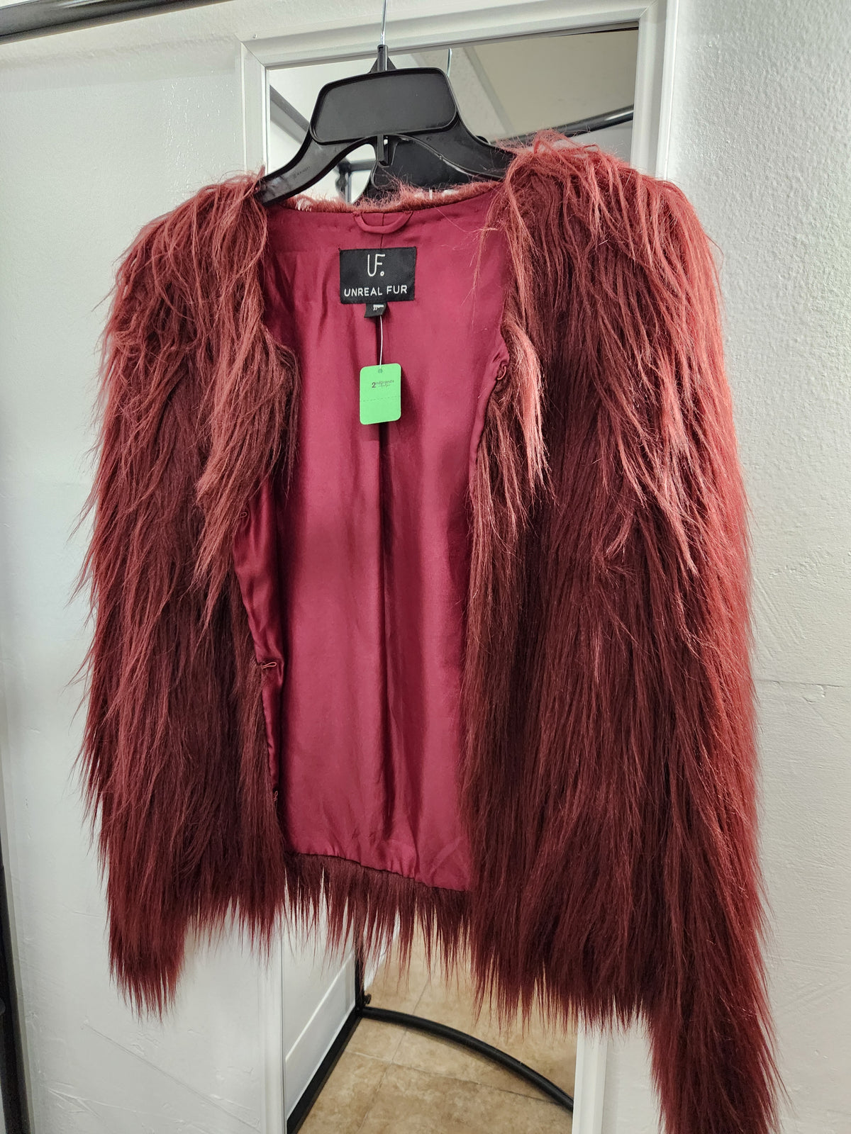 A shaggy, textured burgundy cardigan jacket with a satin lining, hanging on a black hanger in front of a white door