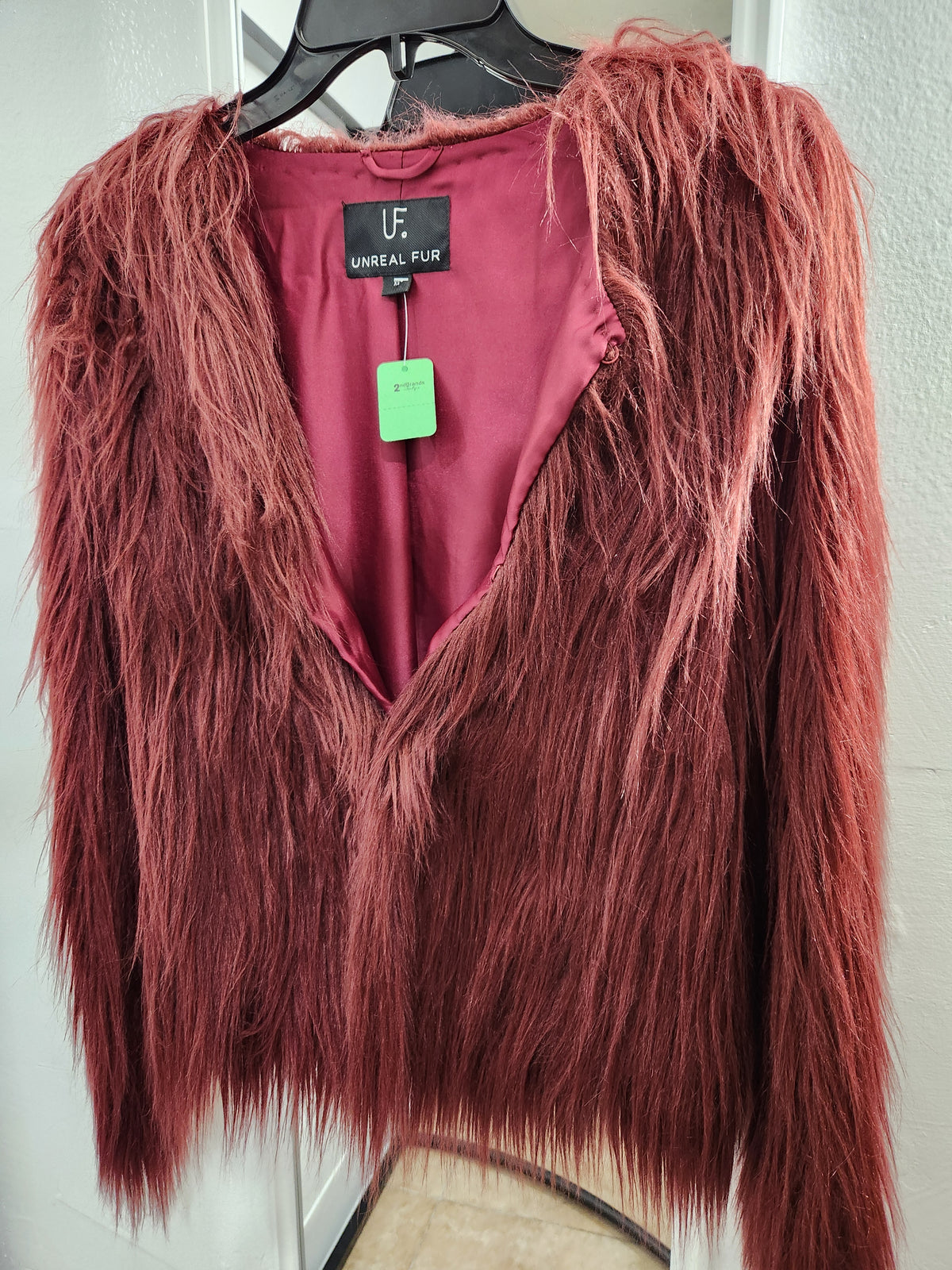 A long-sleeve faux fur vest in a dusty rose or mauve color, hanging on a black hanger against a white wall. The brand label reads 'UNREAL FX'.