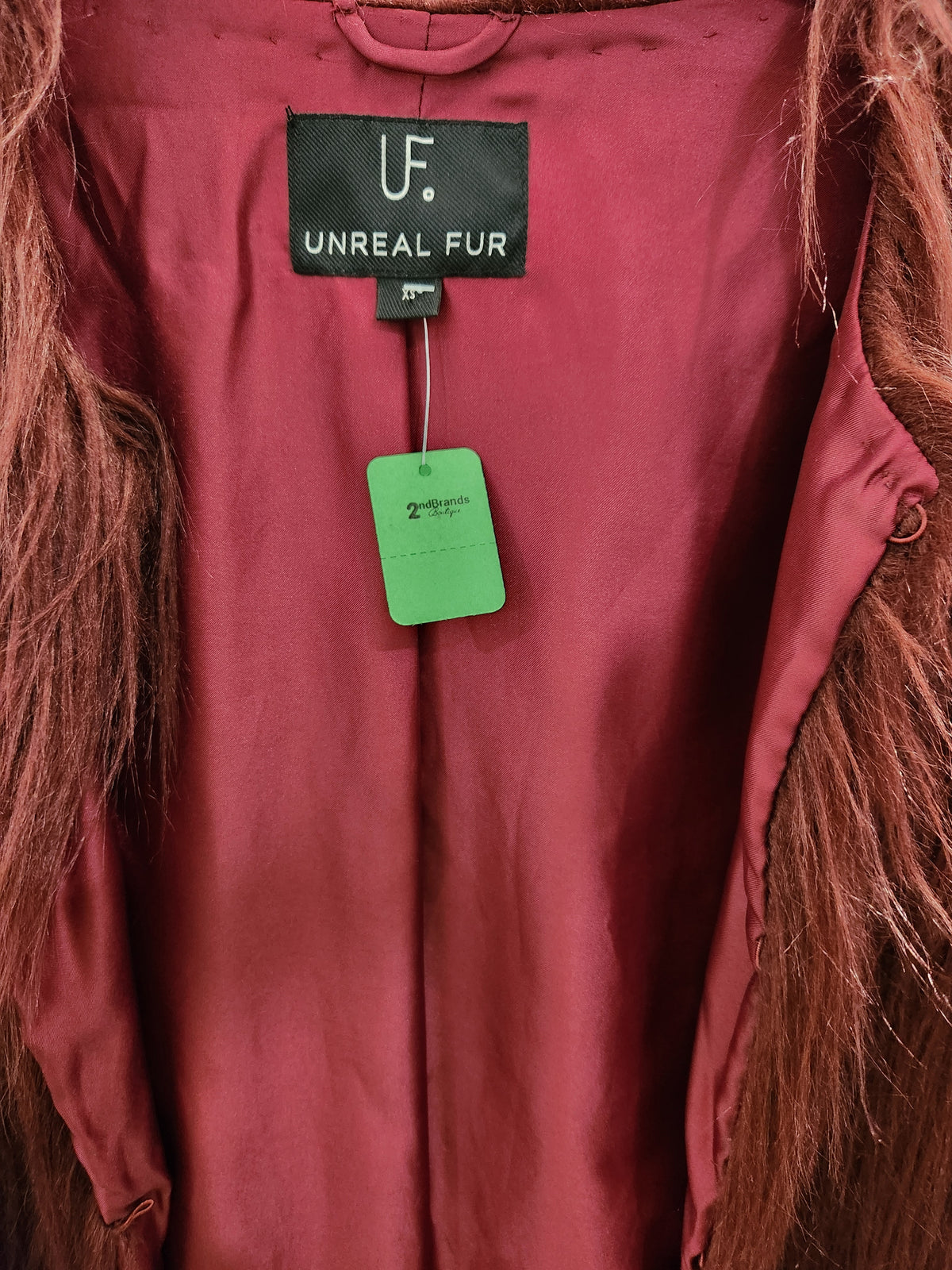 Close-up of a burgundy faux fur vest with a black 'Unreal Fur' brand label and a green hangtag.