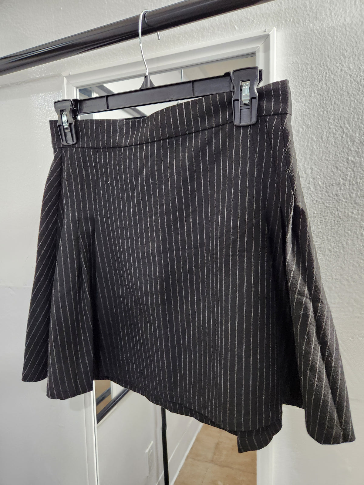 A black pinstriped skirt hanging on a black hanger against a white wall and door frame.