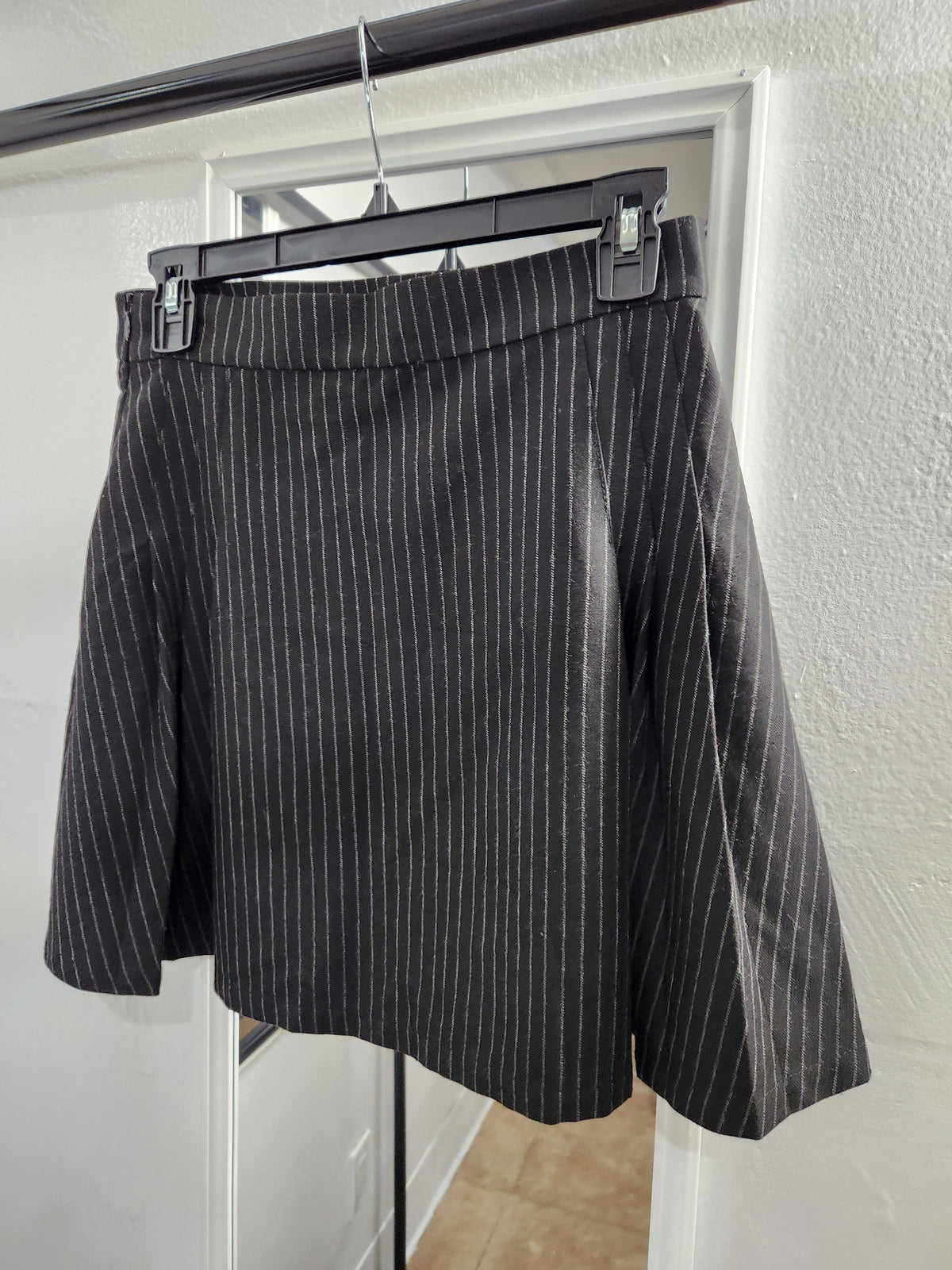 A black pinstriped skirt hanging on a black hanger against a white door frame and textured wall.