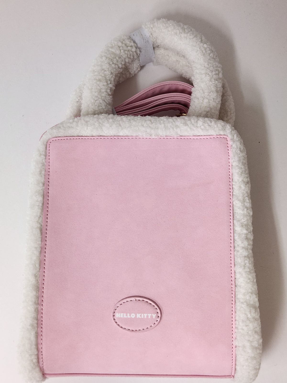 A pink and white fleece handbag with a structured rectangular body, a soft white sherpa handle, and a pink Hello Kitty logo patch on the front.
