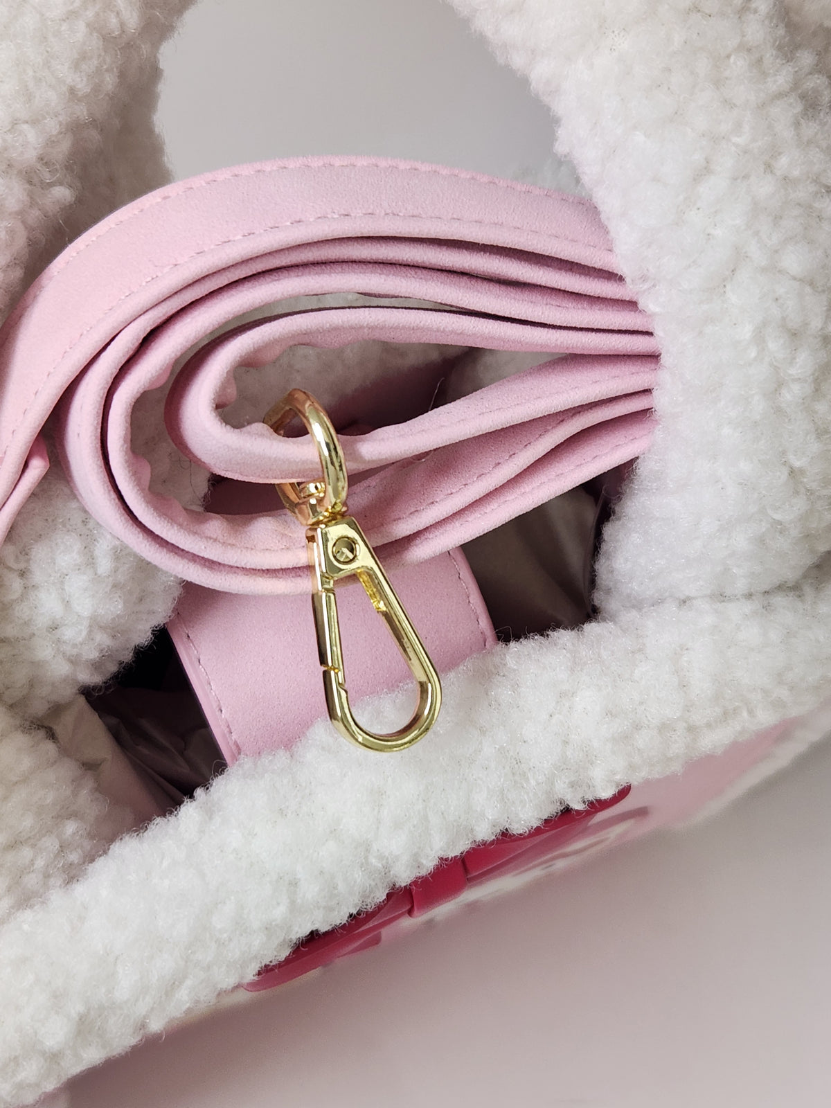Close-up of a light pink faux leather shoulder strap with a gold-tone carabiner clasp, resting inside a white sherpa-lined bag.