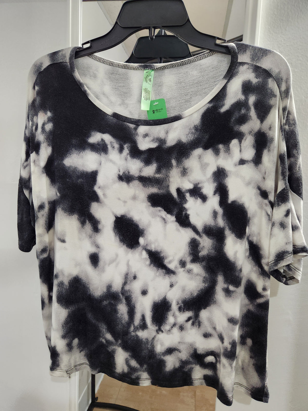 A black and white tie-dye short-sleeve top hanging on a black hanger against a white wall background.