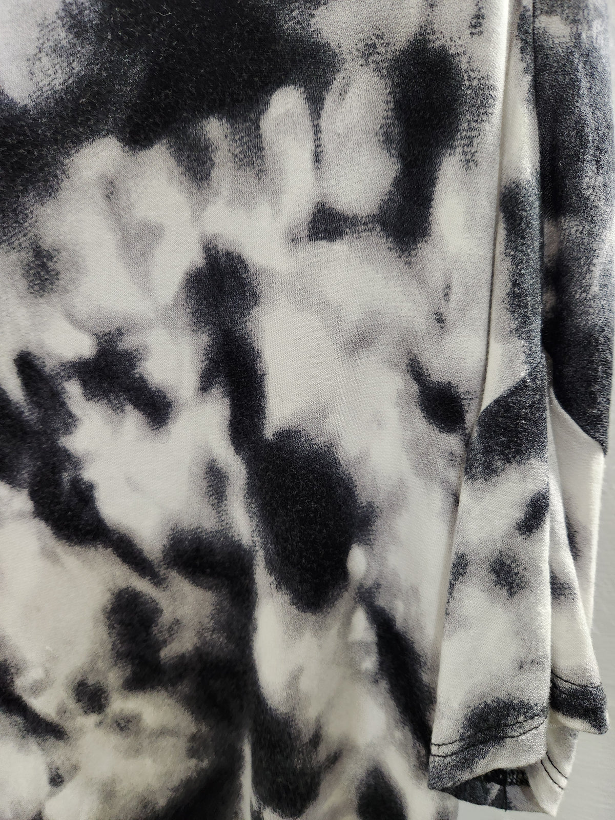 A close-up of a black and white tie-dye patterned fabric, showing the soft texture and drape of the materia.