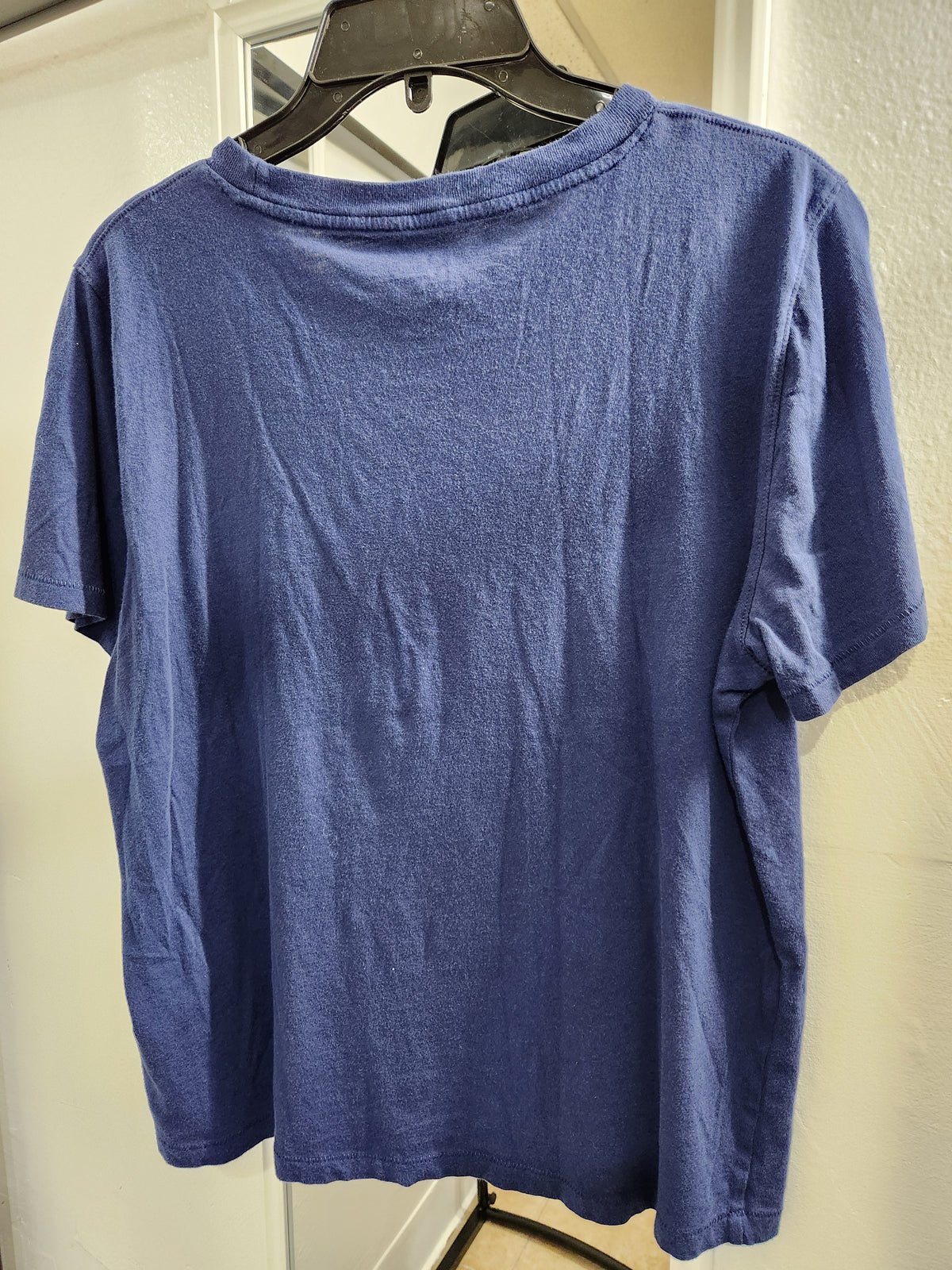 A blue short-sleeve crewneck t-shirt hanging on a black hanger against a white door and textured wall.