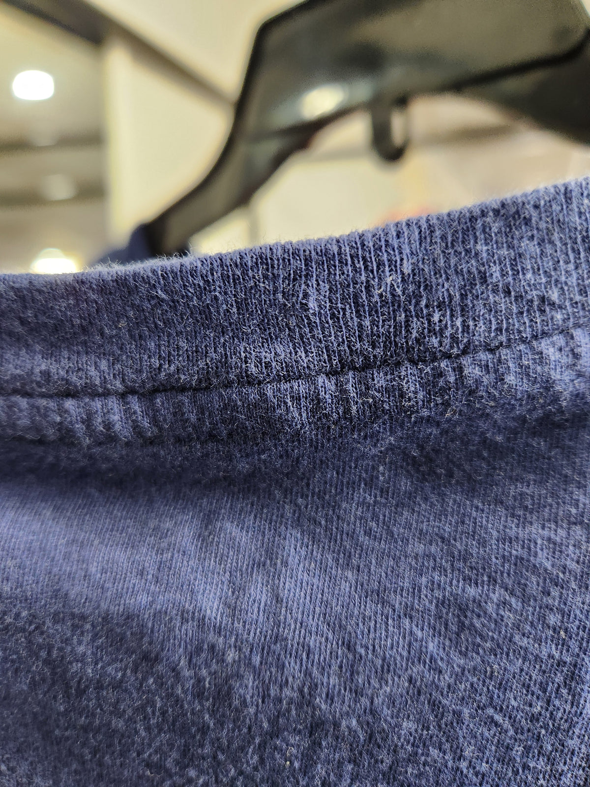 Close-up of a heathered navy blue knit fabric, showing the texture of the collar and ribbed stitching, with a dark hanger and blurred indoor background.