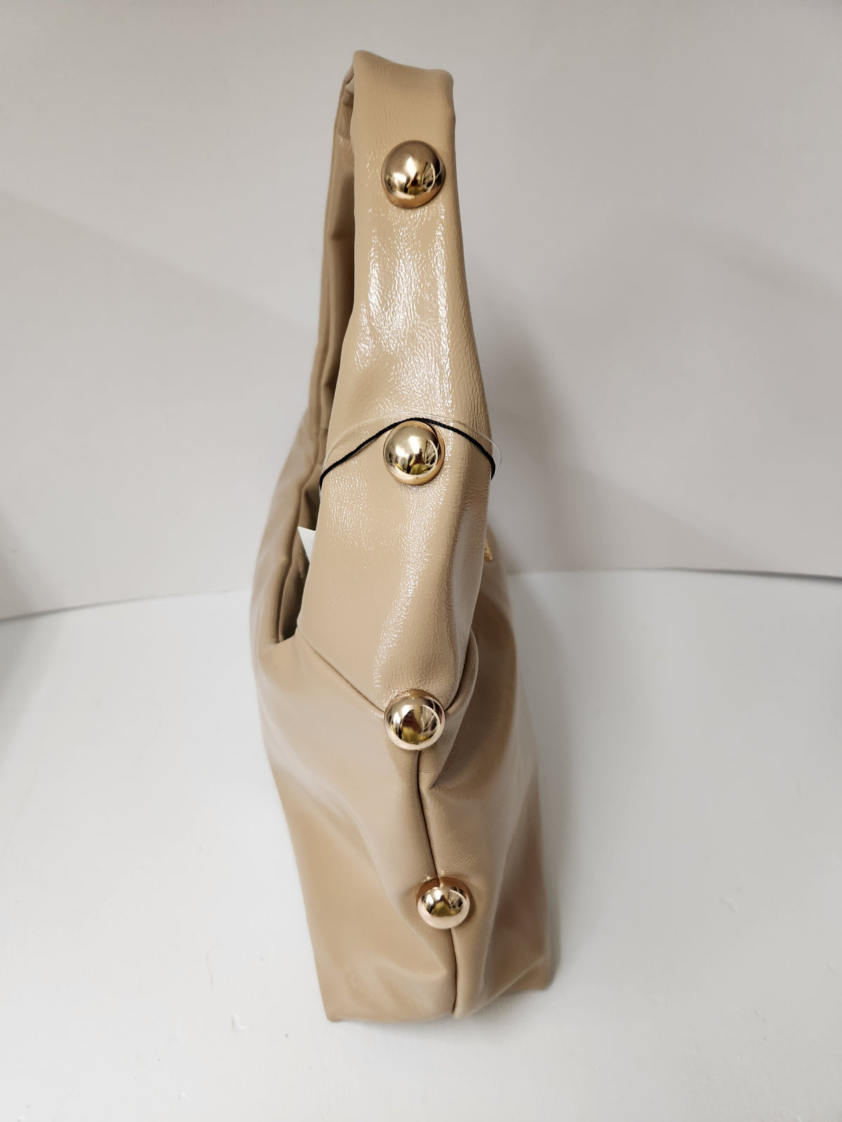A beige leather shoulder bag with a structured, slouchy silhouette and four prominent gold-tone metal studs down the front, shown against a plain white background.
