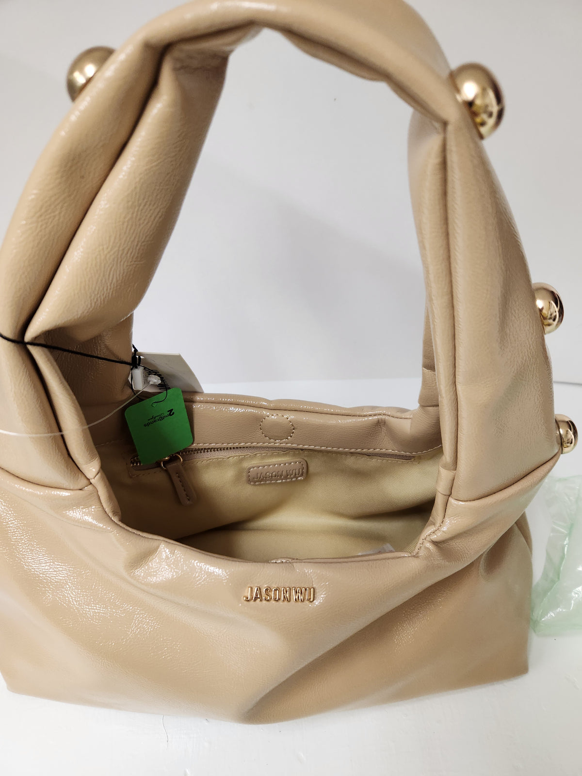 A beige leather shoulder bag with gold-tone decorative hardware and a green hangtag, shown open to reveal the interior.