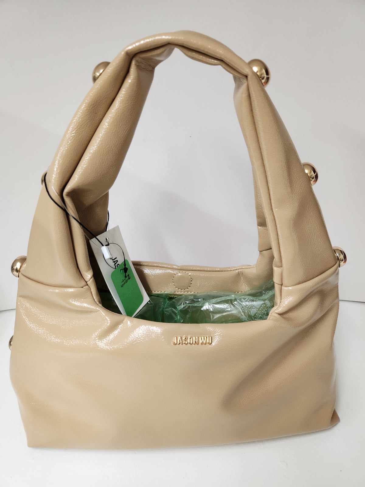 A beige leather shoulder bag with gold-tone metal accents and a hangtag, photographed against a plain white background.