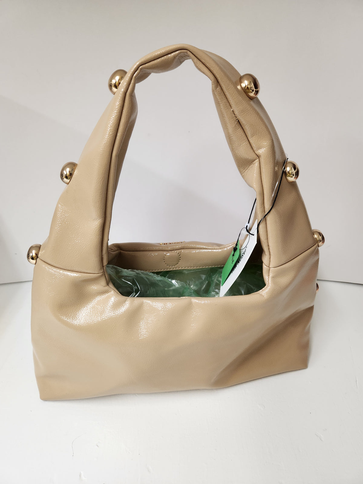 A beige faux-leather shoulder bag with gold-tone decorative knobs on the handle and side, shown with a green interior lining and a white product tag.