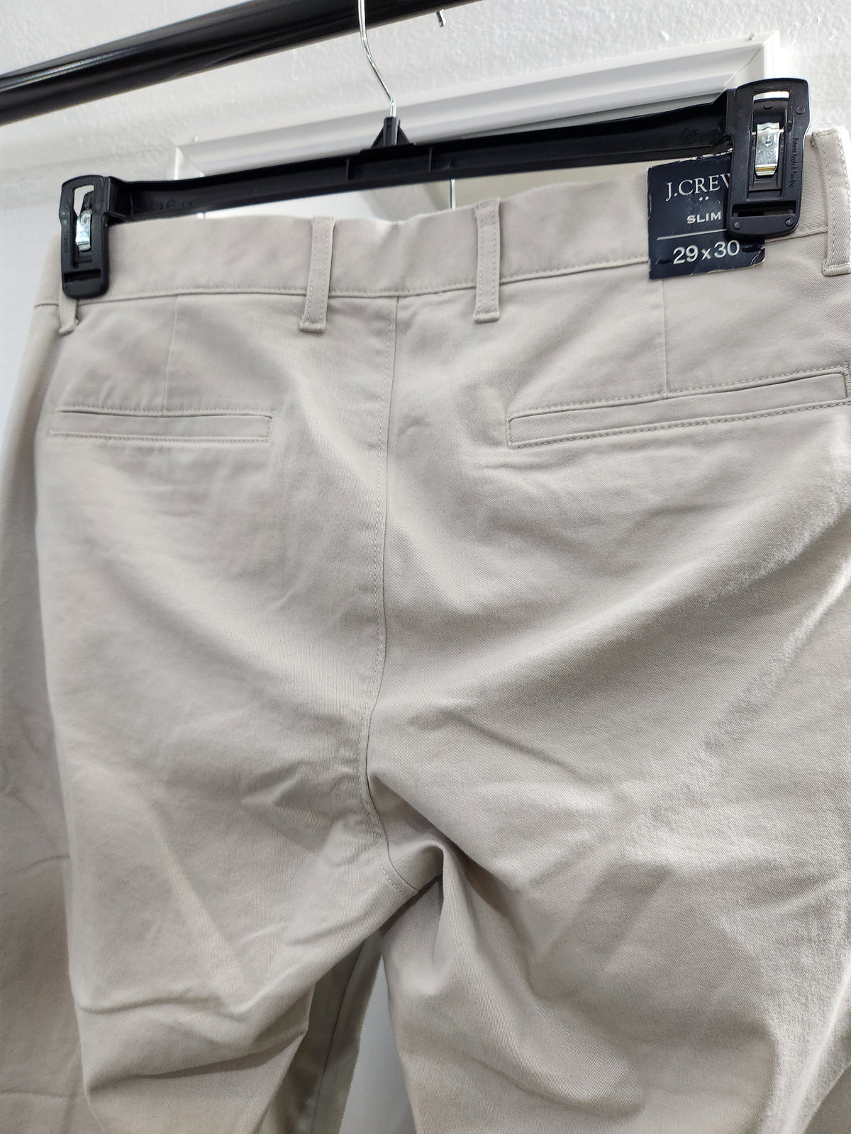J.Crew Slim 29 x 30 beige chino pants hanging on a black hanger, showing the back waistband, belt loops, and rear pockets.