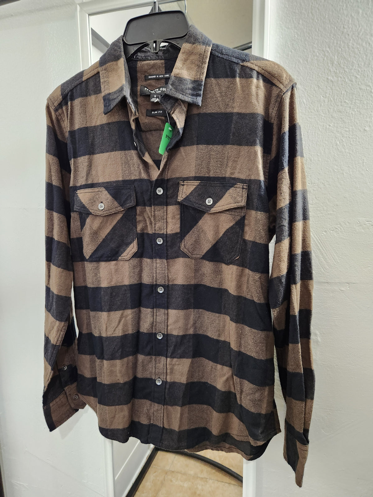 A long-sleeve button-up shirt with diagonal brown and black stripes, hanging on a black hanger against a white door and wall.