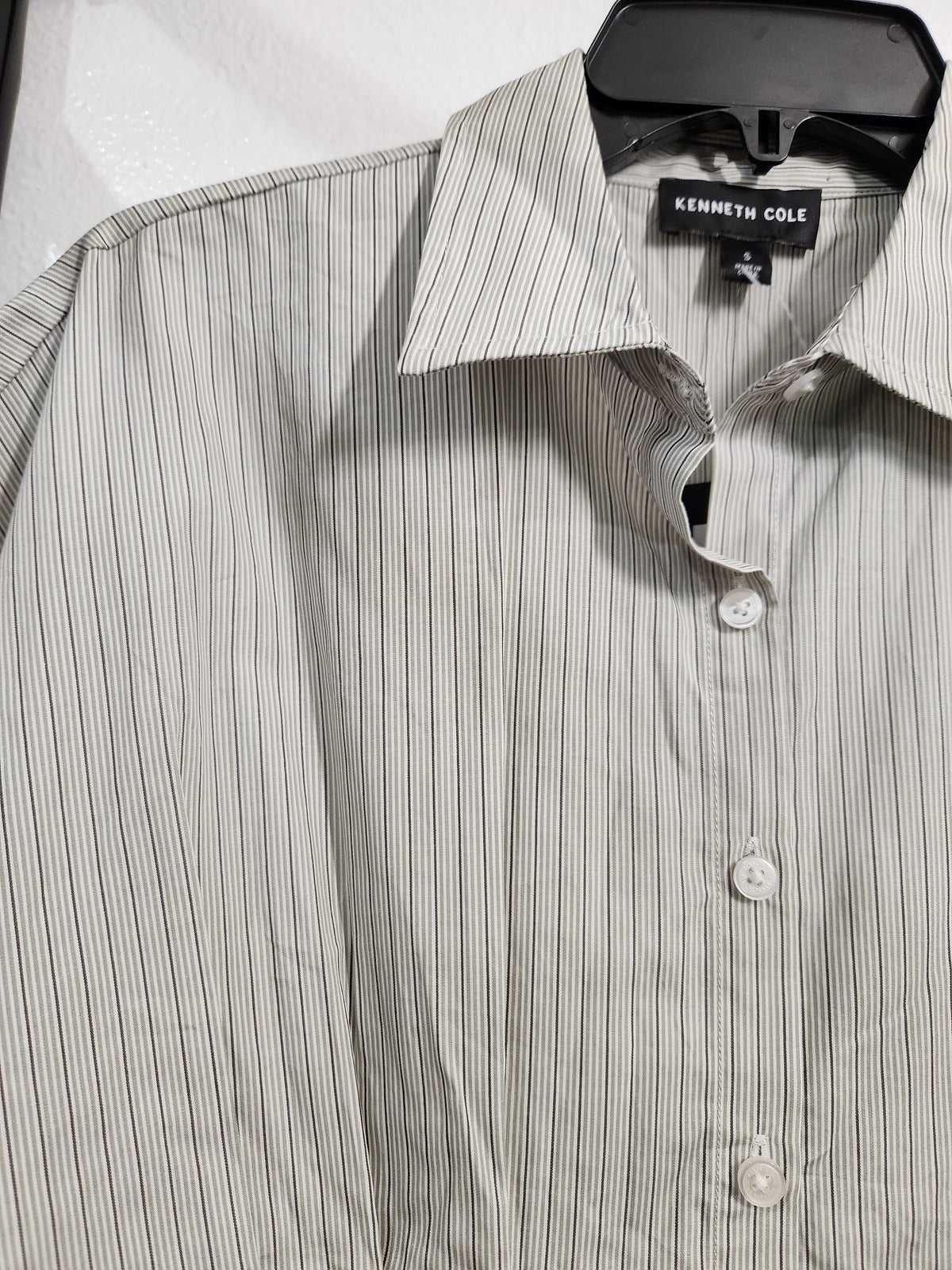A close-up of a Kenneth Cole button-down shirt with thin vertical stripes in beige and gray, hanging on a black hanger.