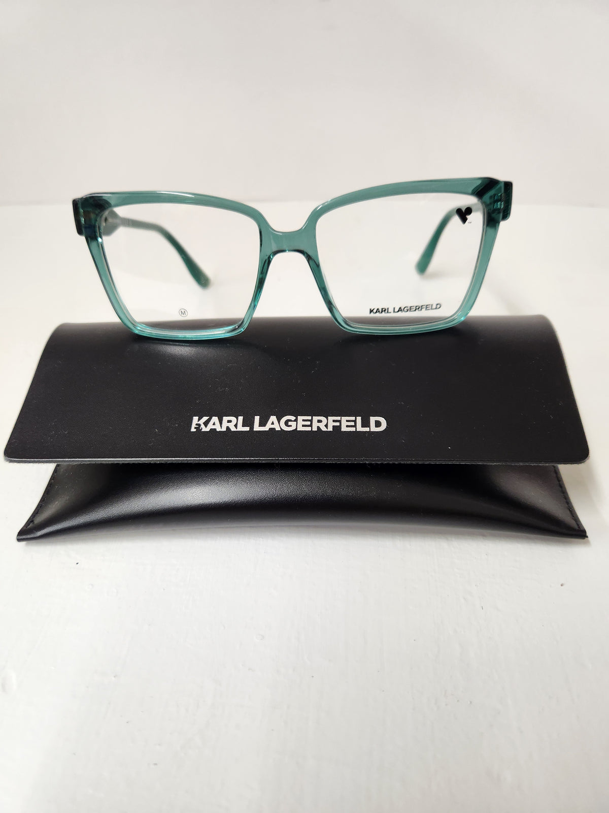 Karl Lagerfeld eyeglasses with translucent teal-green frames, displayed on top of a black branded hard case against a white background.