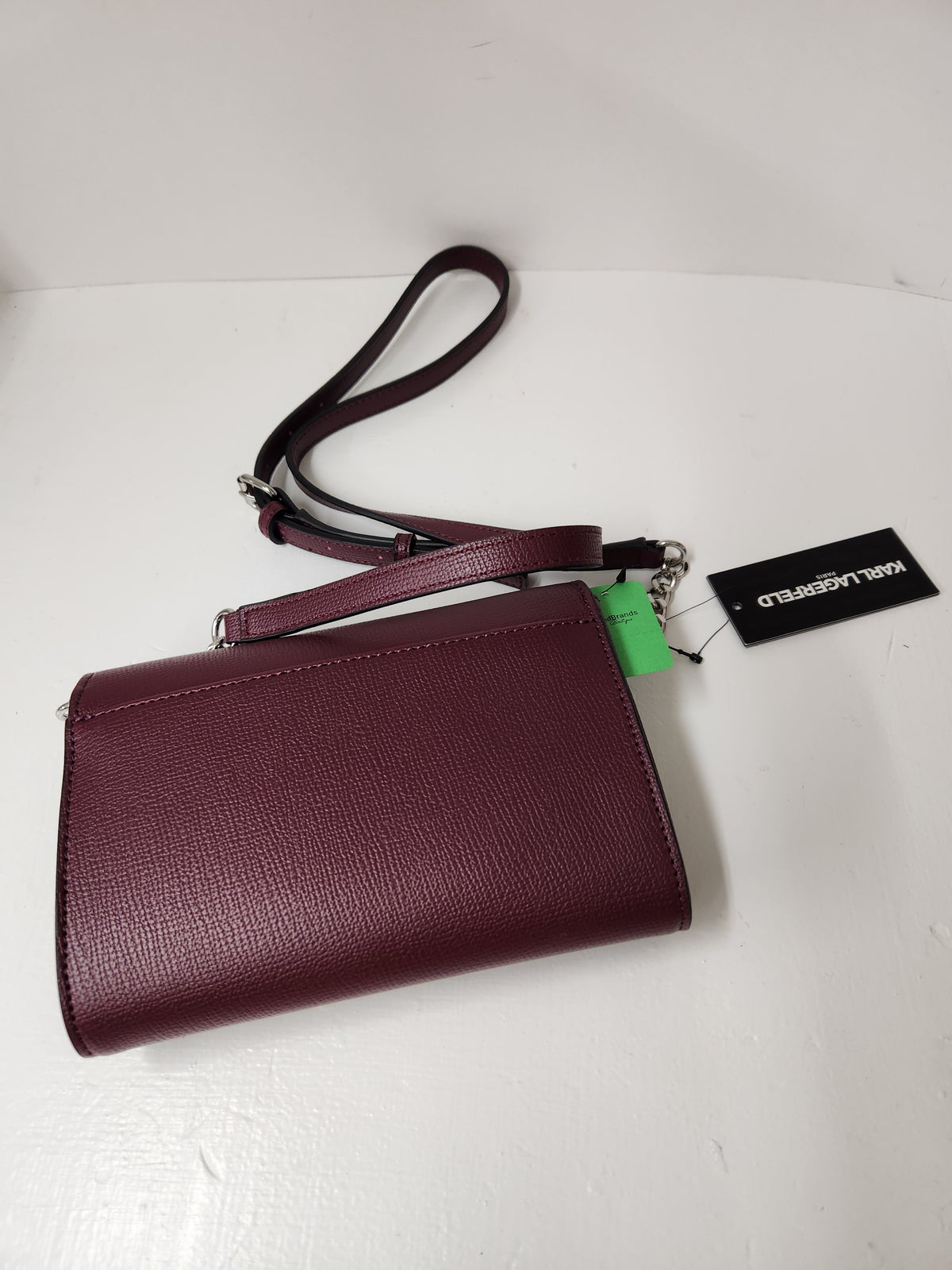 A burgundy pebbled leather crossbody bag with a matching adjustable strap, shown with a green hangtag and a black brand tag on a white surface.