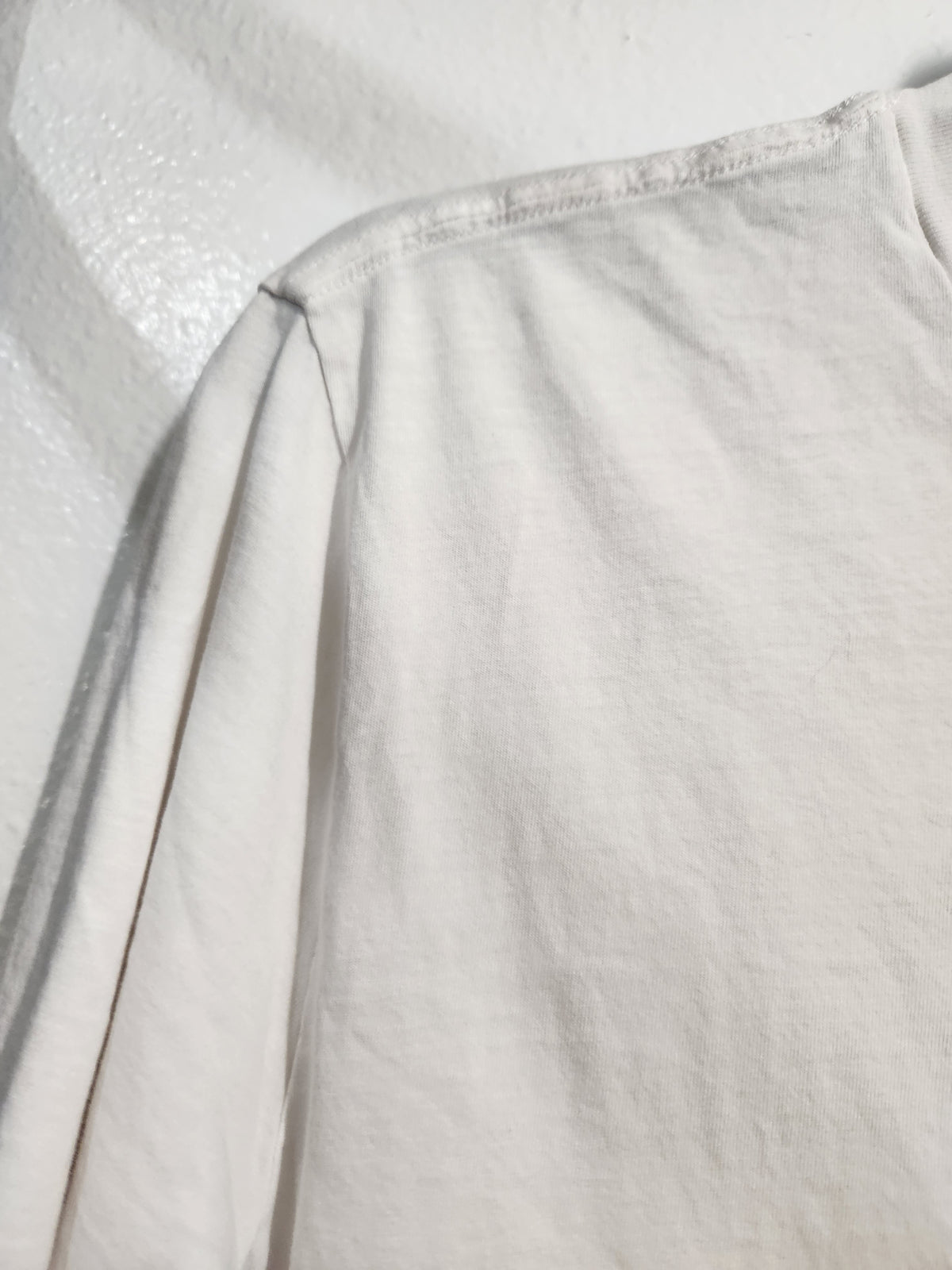 Close-up of a light off-white or cream-colored fabric garment, showing the shoulder seam and textured material.
