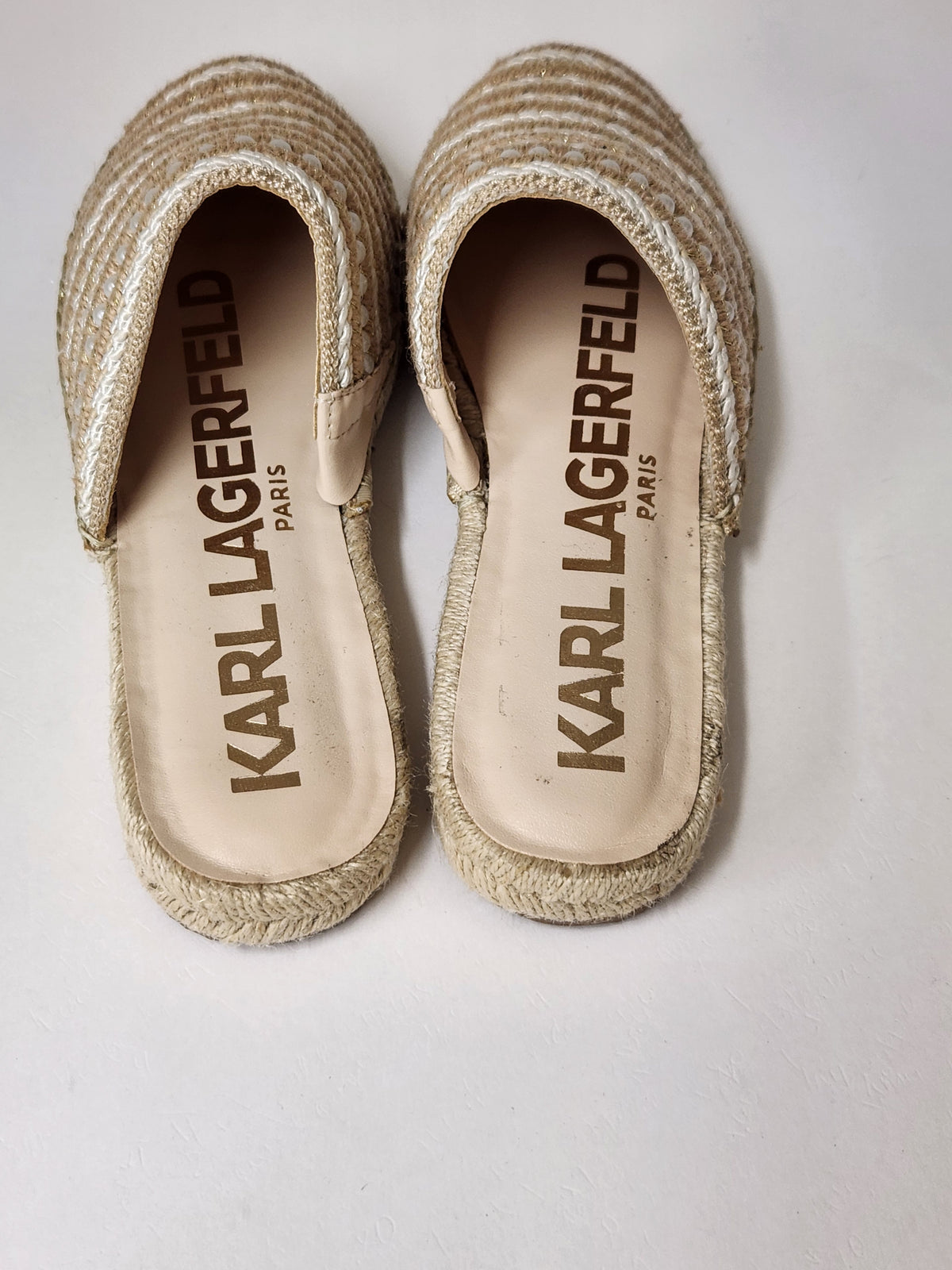 A pair of Karl Lagerfeld Paris espadrille mule sandals with woven beige jute uppers and beige insoles featuring the brand name printed in brown.