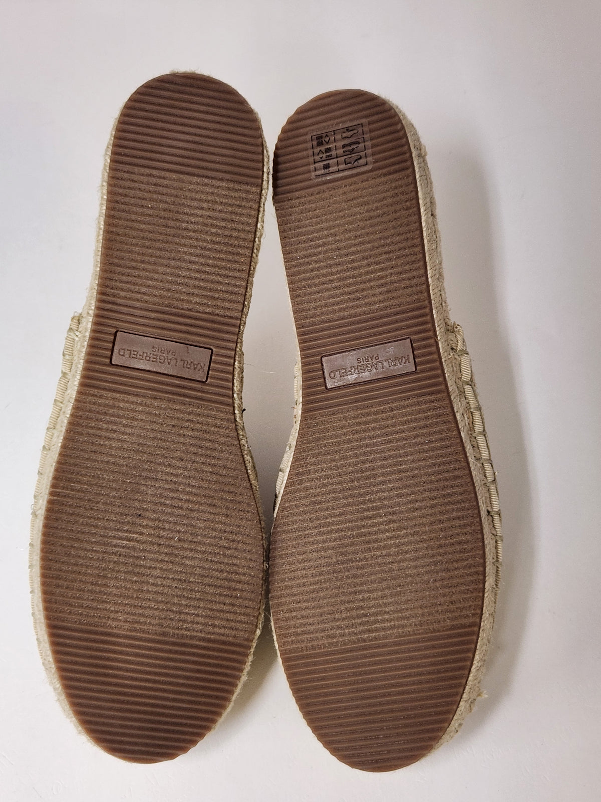 A pair of espadrille flat shoes shown from the sole side, featuring brown textured rubber soles and a natural beige jute-wrapped edge, photographed on a plain white background.