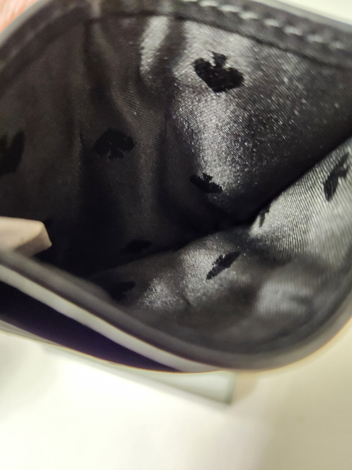 Close-up of the interior lining of a black wallet or pouch, showing a satin-like black fabric with a repeating small heart pattern.