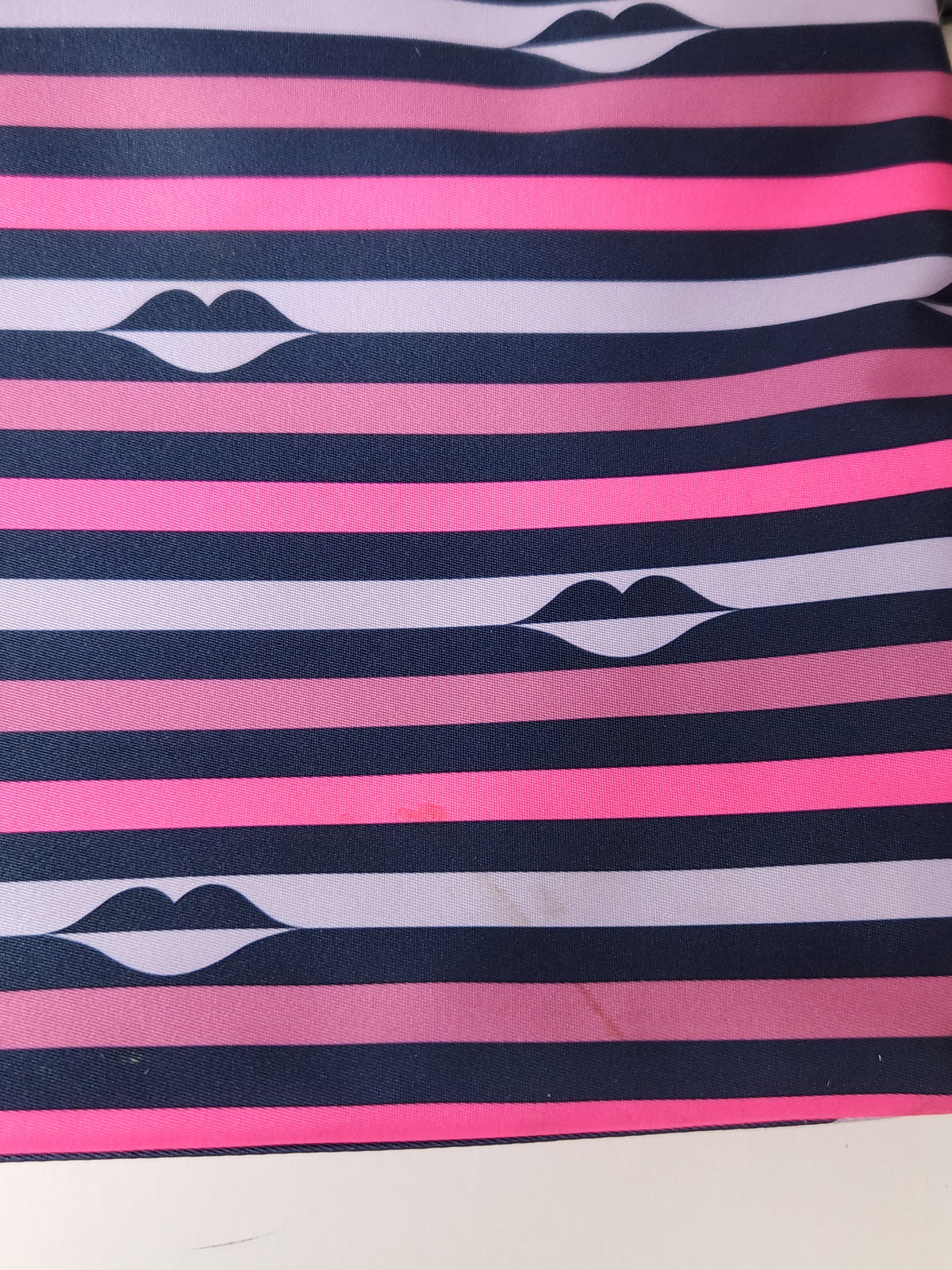 A close-up of a striped fabric or wallpaper pattern featuring alternating dark navy, bright pink, and light lavender horizontal stripes, with a stylized black-and-white lips motif centered on each stripe.