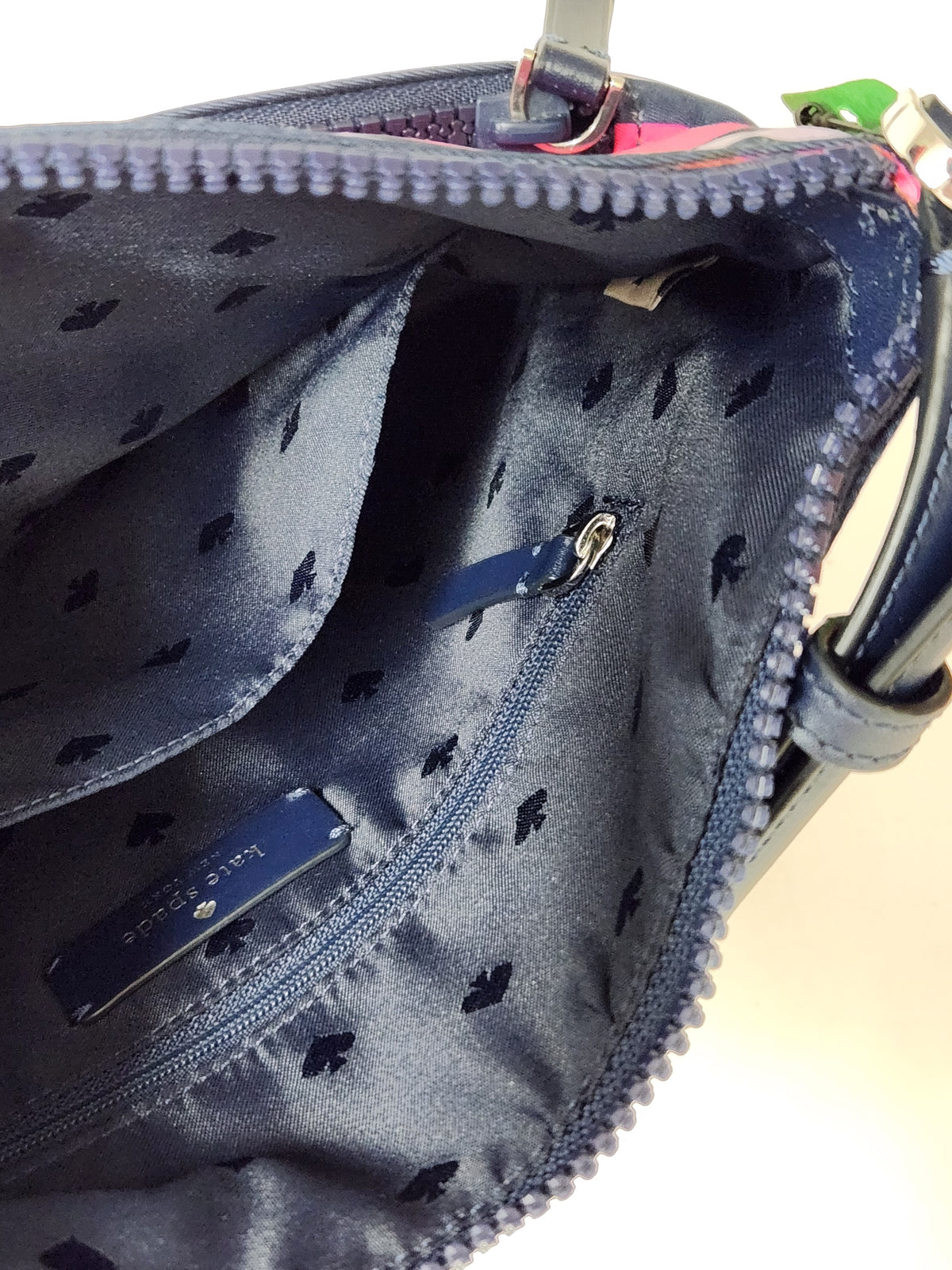 Close-up of the interior of a navy blue handbag with a repeating small black floral pattern, a zippered pocket, and a blue brand tag.