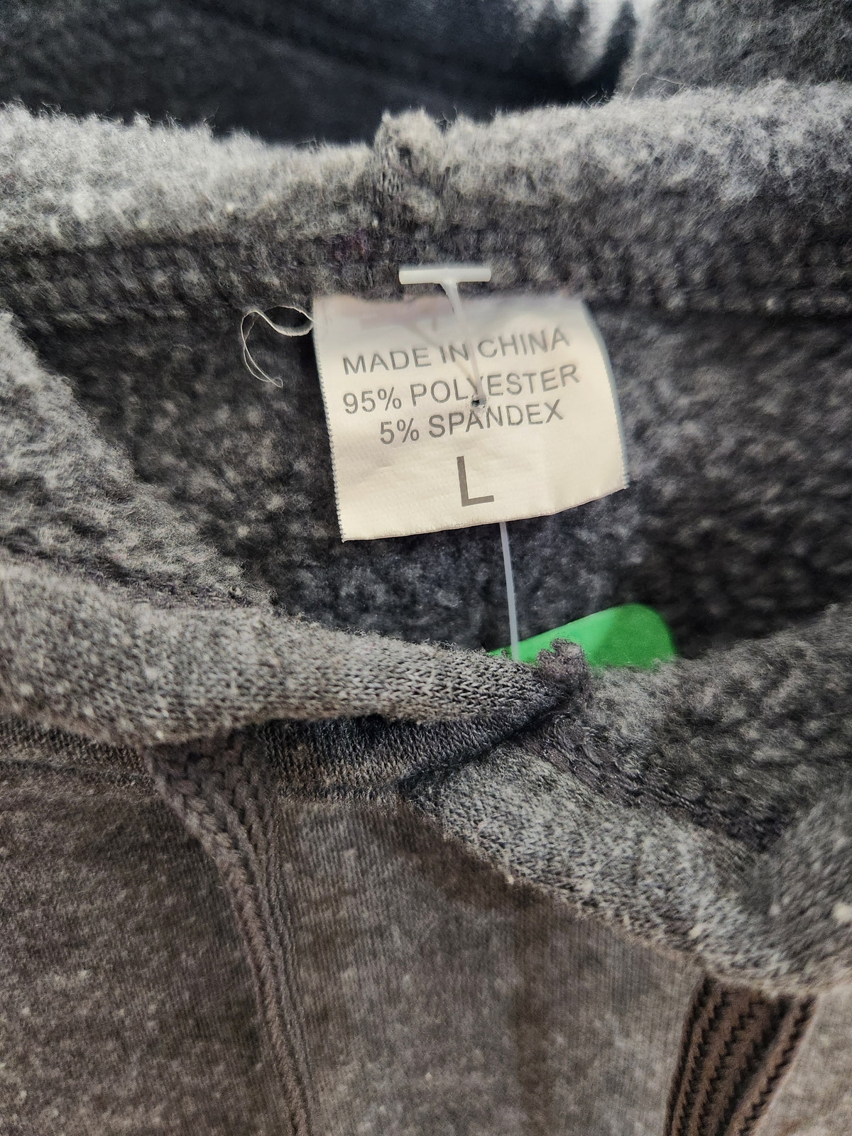 Close-up of a gray knit garment showing the inside neck label with text reading 'MADE IN CHINA 95% POLYESTER 5% SPANDEX' and size 'L'.