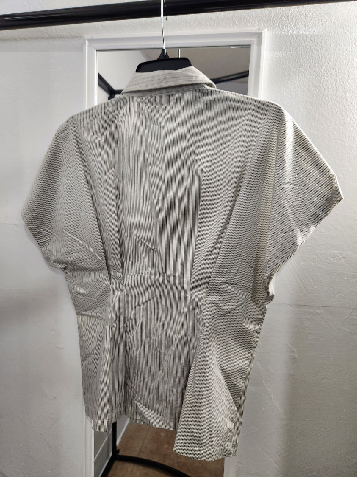 A light gray and white vertically striped short-sleeve button-up shirt hanging on a black hanger against a white wall.