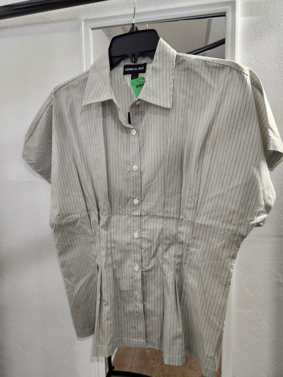 A short-sleeve button-up shirt with vertical pinstripes, hanging on a black hanger against a white door frame.