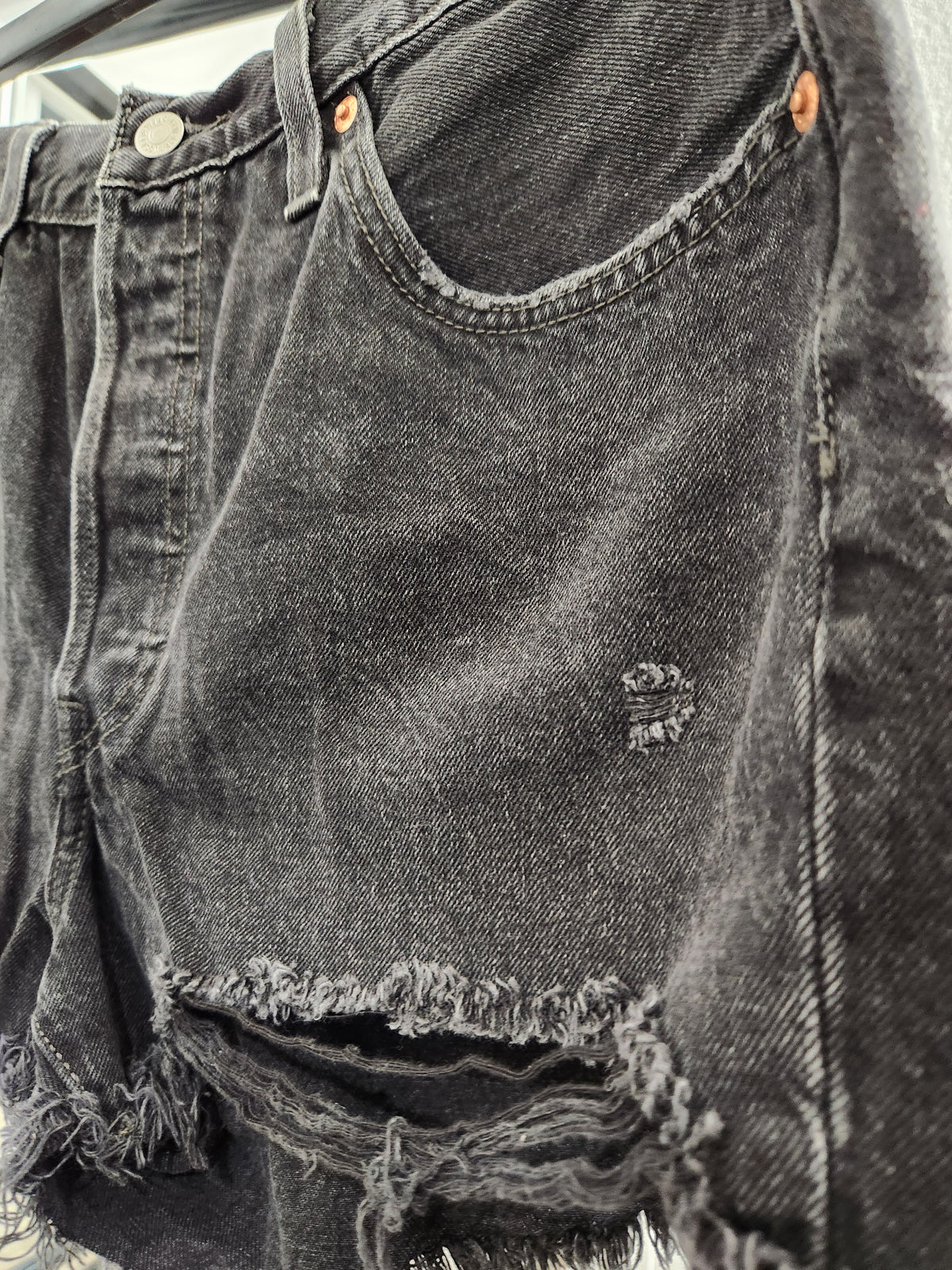 Close-up of a pair of dark gray washed denim shorts with a distressed, frayed hem and a small ripped detail on the front.