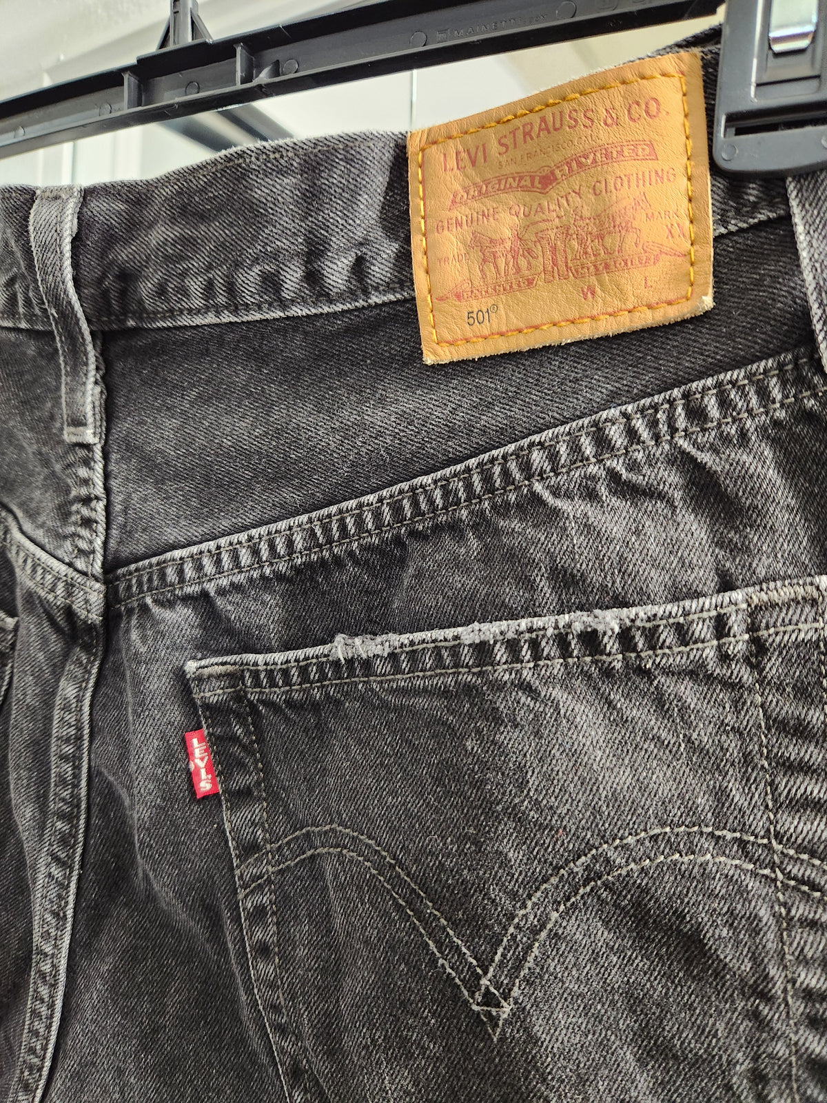 Close-up of the back waistband and pocket area of dark gray washed Levi's jeans hanging on a black hanger. The tan leather brand patch is visible at the back waist, and a small red Levi's tab is visible on the pocket.