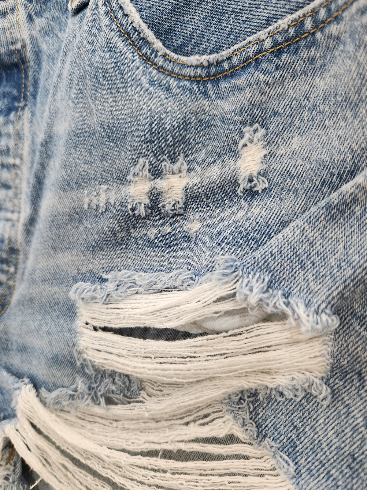 Close-up of light blue distressed denim fabric with frayed holes and raw edges.