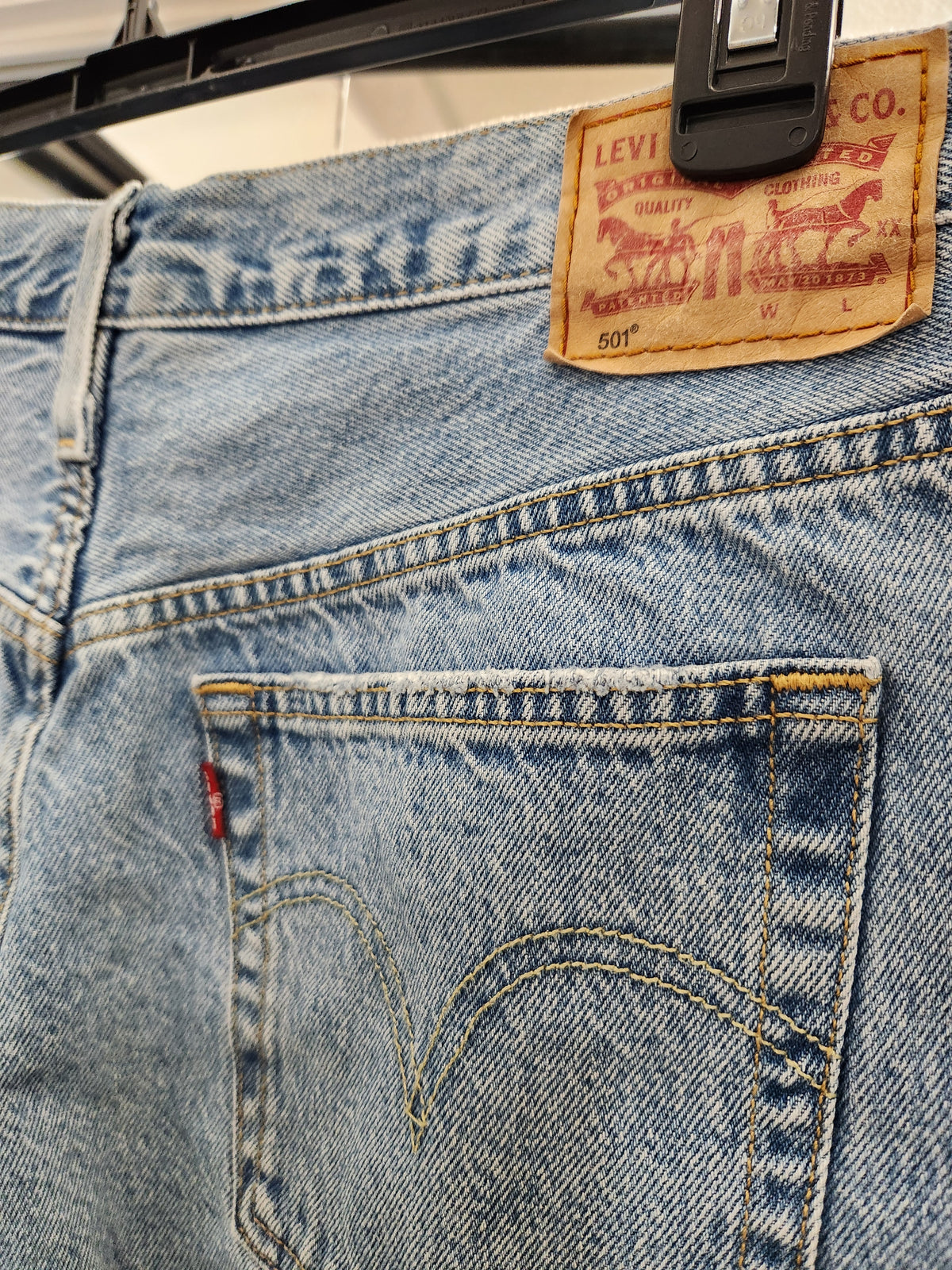Close-up of the back waistband and right back pocket of light-wash blue Levi's jeans, showing the tan leather brand patch and red tab detail.
