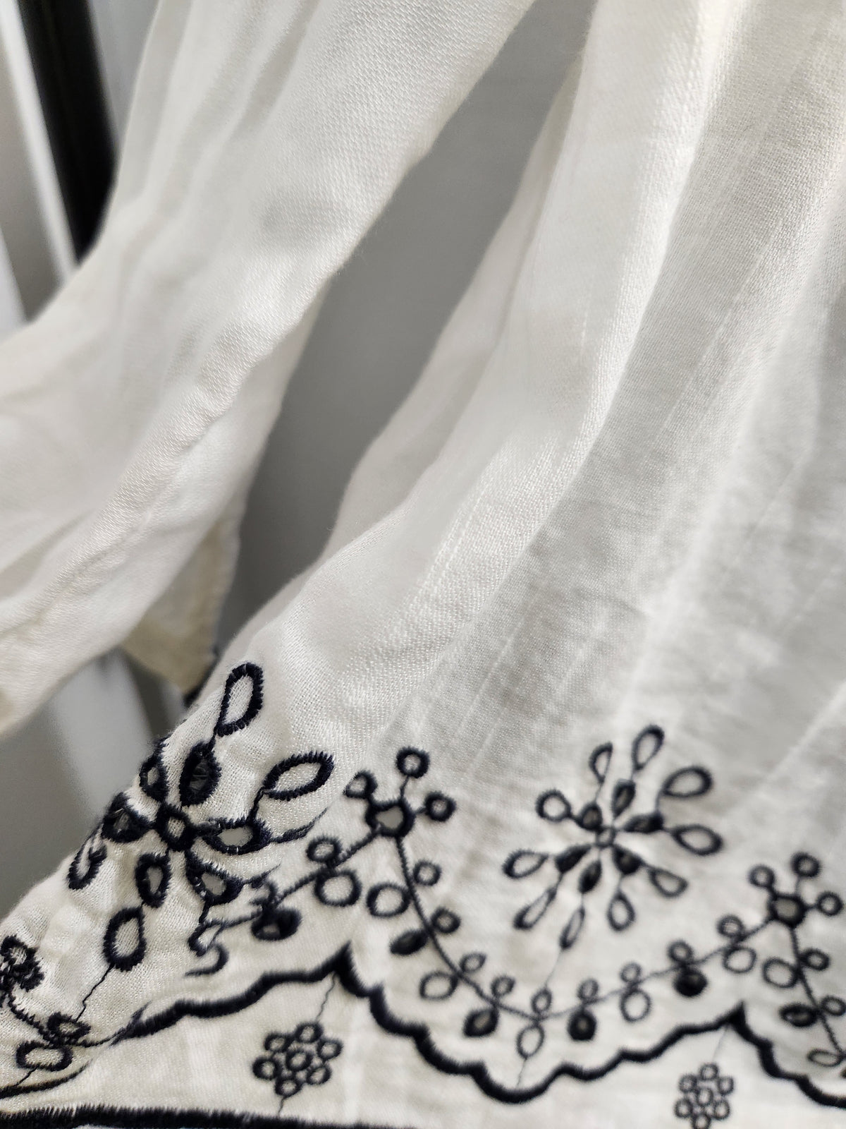 Close-up of a white sheer fabric with black floral embroidery along the hem.