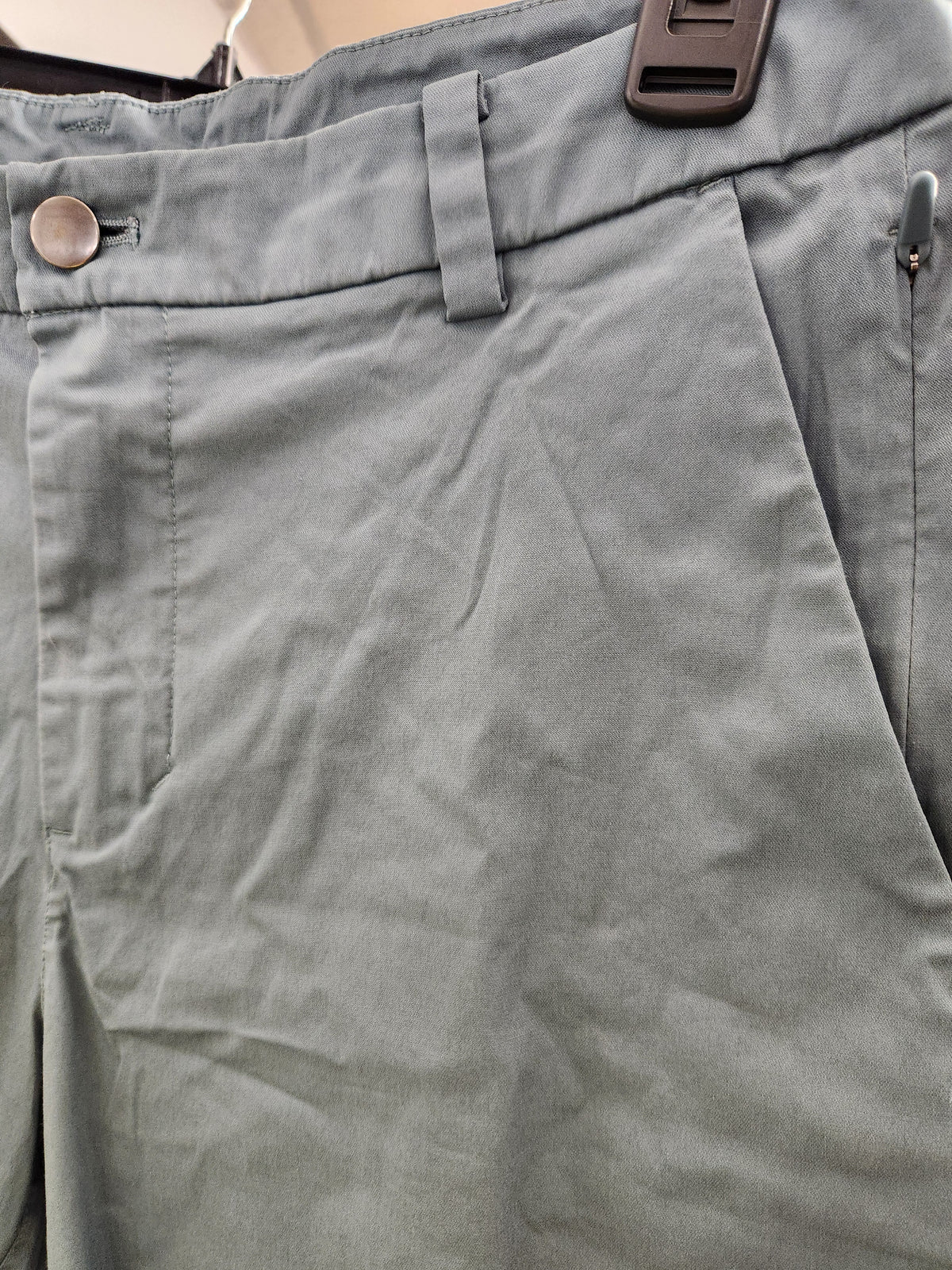 Close-up of the waistband of light gray trousers, showing a button closure, belt loops, and a dark plastic belt buckle.