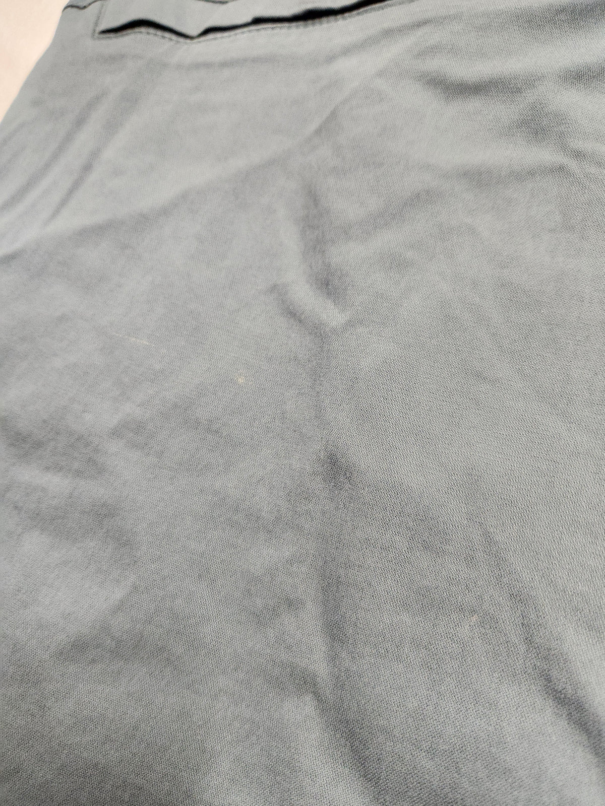 A close-up of a light gray fabric surface with visible wrinkles and a small portion of a dark waistband at the top edge.